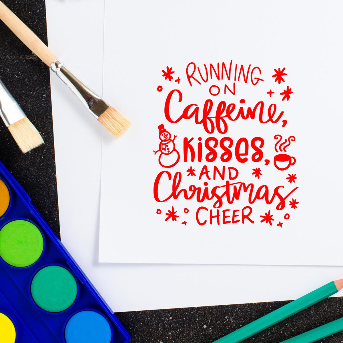 Red Christmas stamp and seal reading Running on Caffeine, Kisses, and Christmas Cheer, with paintbrushes and watercolor palette.