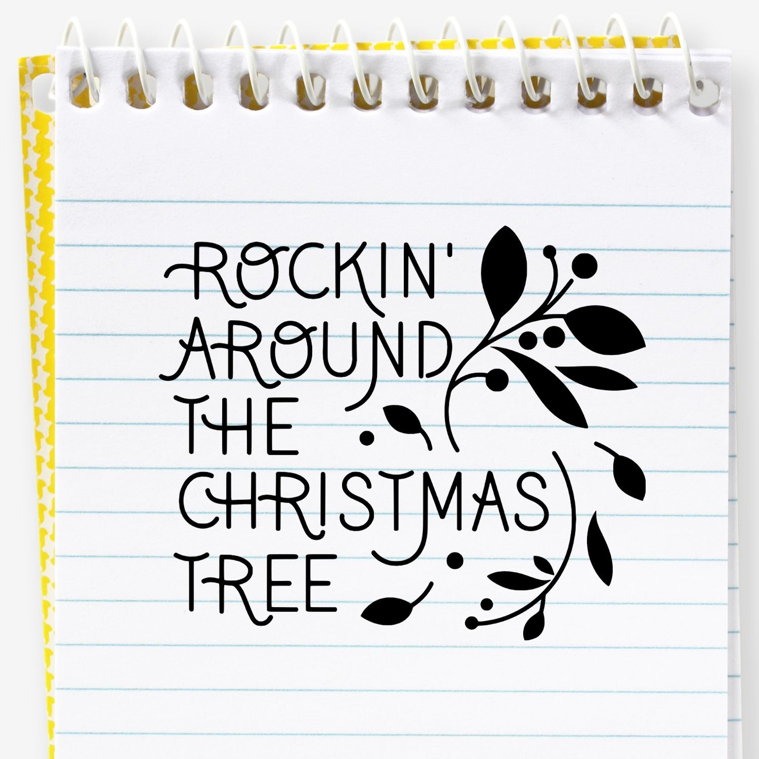 Holiday stamp design with black Rockin Around the Christmas Tree text, floral flourish, on white lined notepad with yellow border.