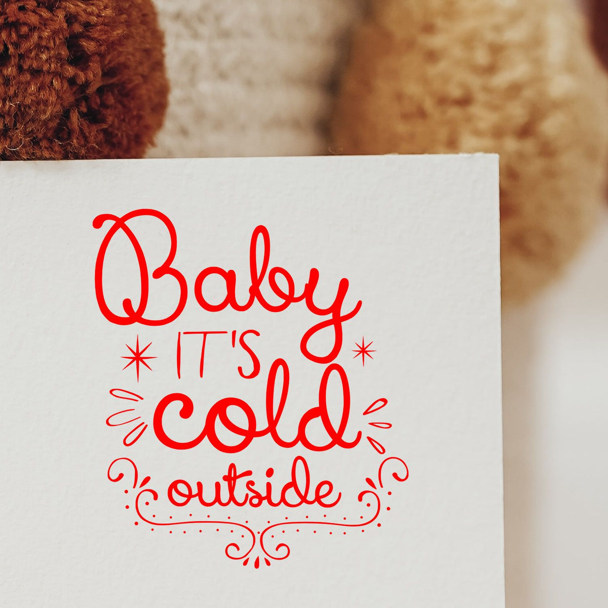 Red decorative stamp seal reading Baby its cold outside on white paper, with playful swirls and star accents.