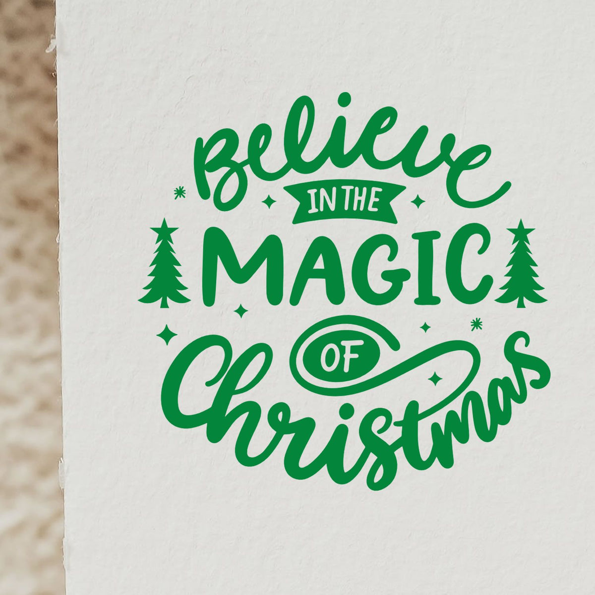 Green holiday stamp/seal reading Believe in the Magic of Christmas with trees, stars, and white background.