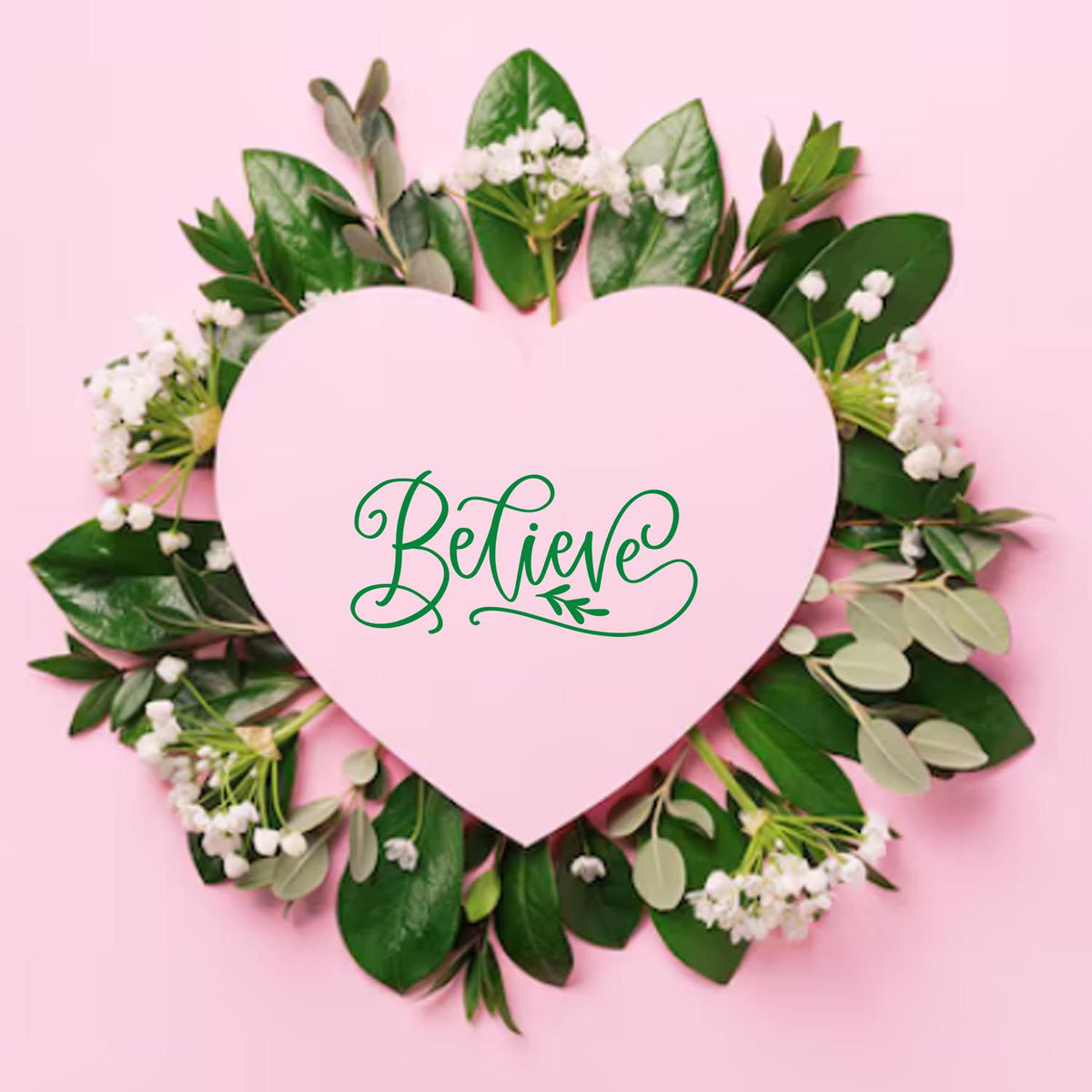 Pink heart seal stamp with green Believe script, surrounded by leafy wreath and small white flowers on a pastel pink background.