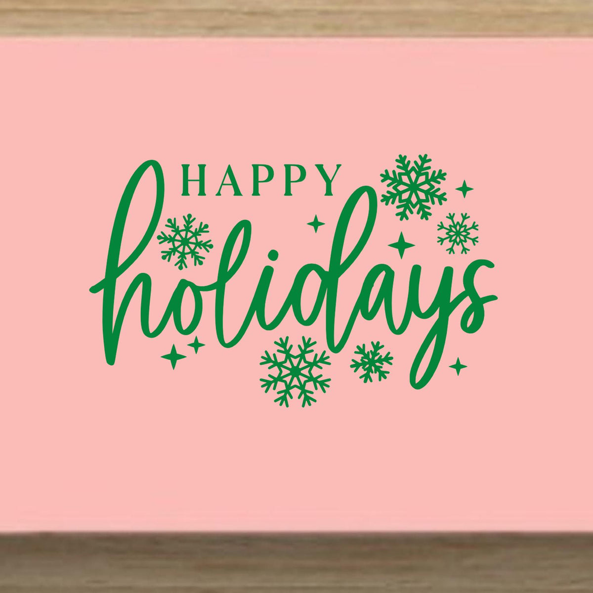 Green Happy Holidays stamp and seal with snowflakes and sparkles on a pink background.