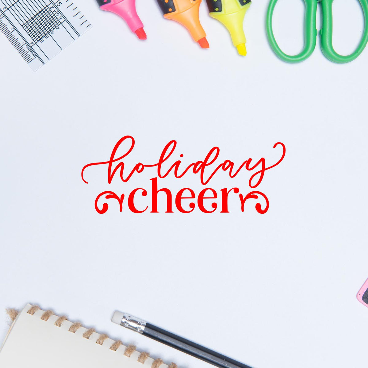Red holiday cheers stamp for seal products, surrounded by pink, orange and yellow markers, green scissors, ruler, notebook and pencil.