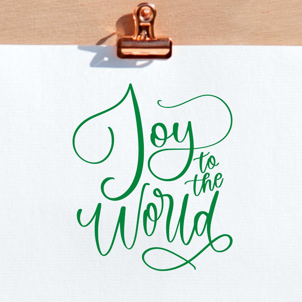 Green script stamp and seal reading Joy to the World on white paper, clipped with a copper binder clip.