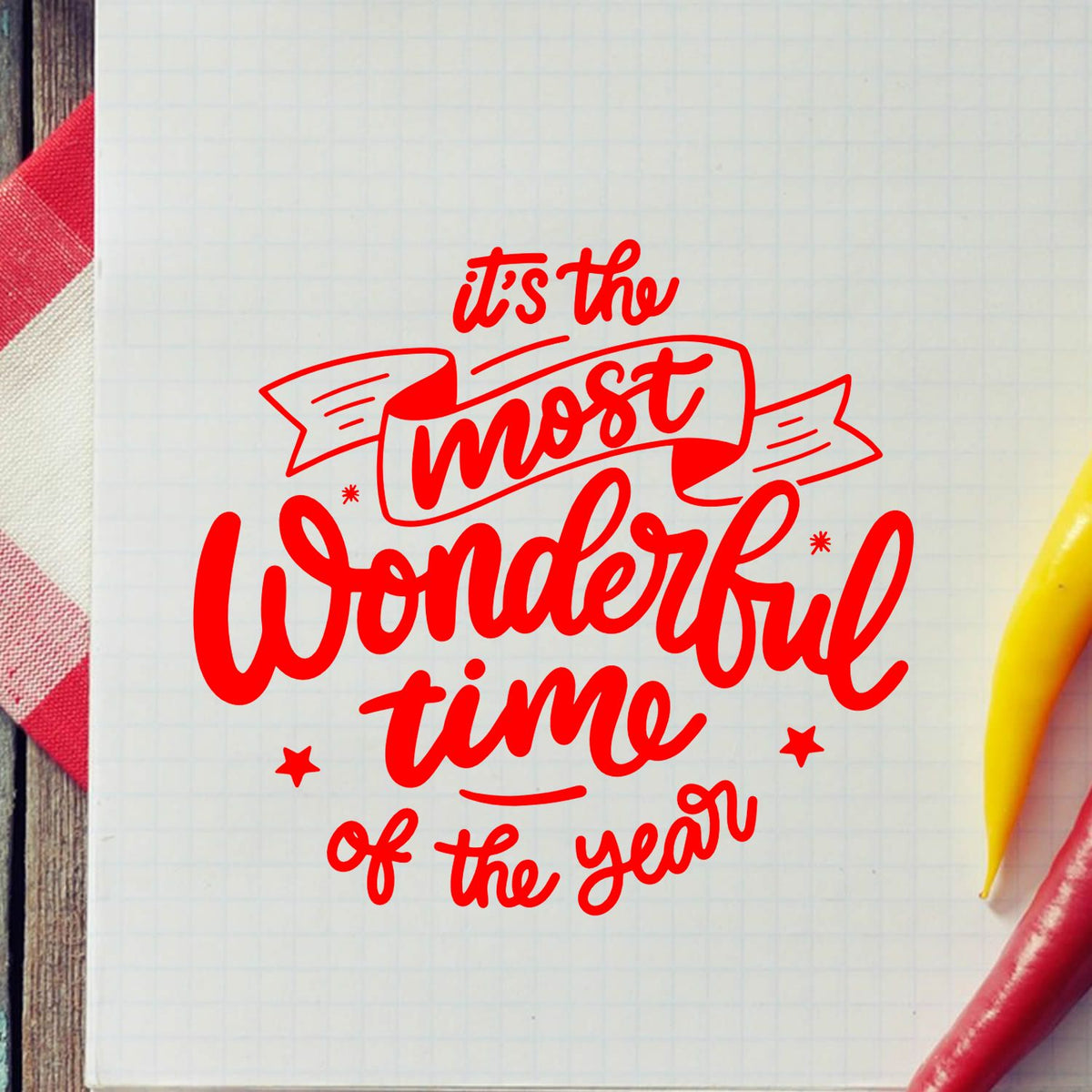 Red decorative stamp seal with its the most wonderful time of the year on white grid paper, with red and yellow pens.