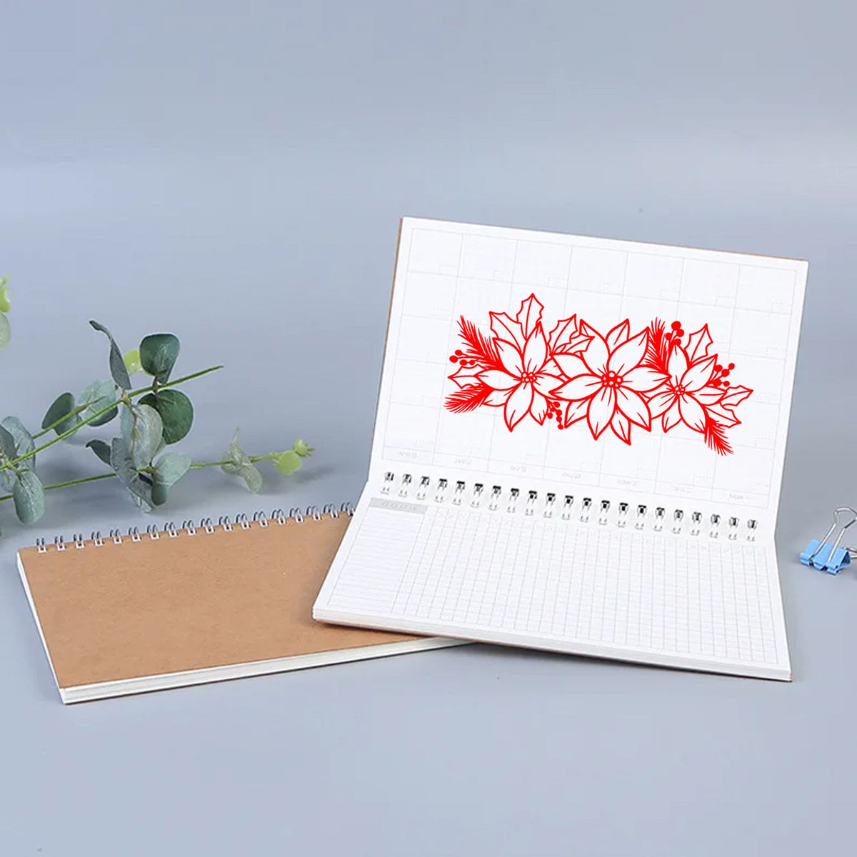 White grid notebook featuring a red floral stamp-and-seal design, beside a brown spiral notebook on a gray background.