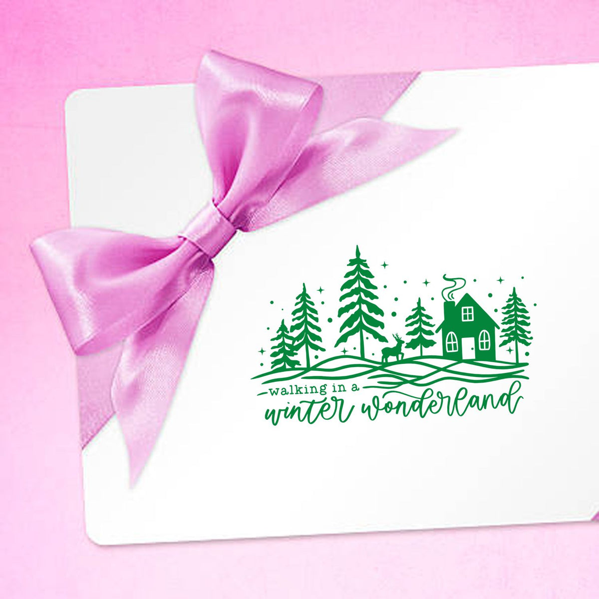 White card with pink satin bow and green winter wonderland stamp seal featuring trees, house and deer.