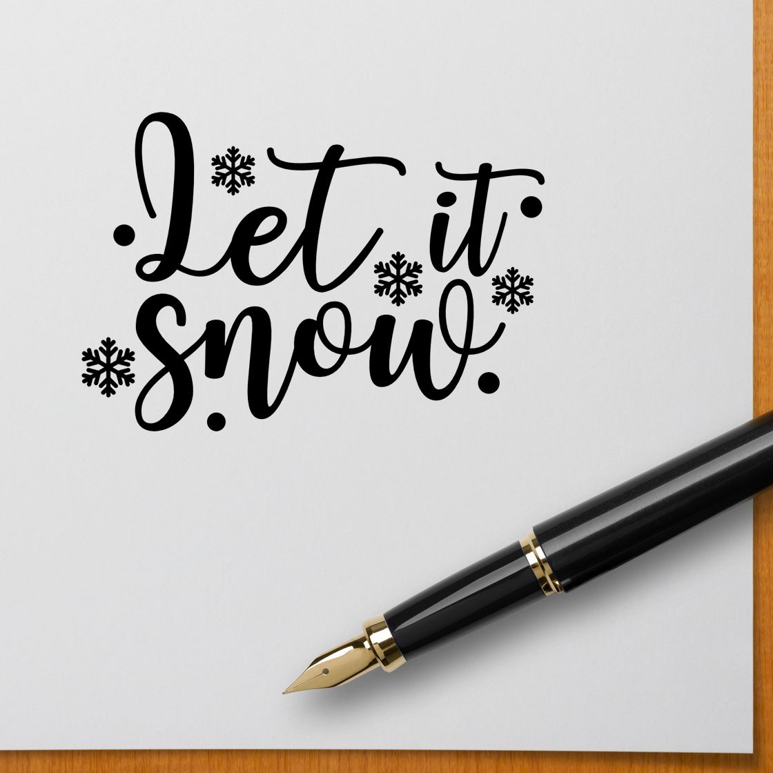 Black Let it snow stamp with snowflakes on white paper, beside a black fountain pen with gold nib.