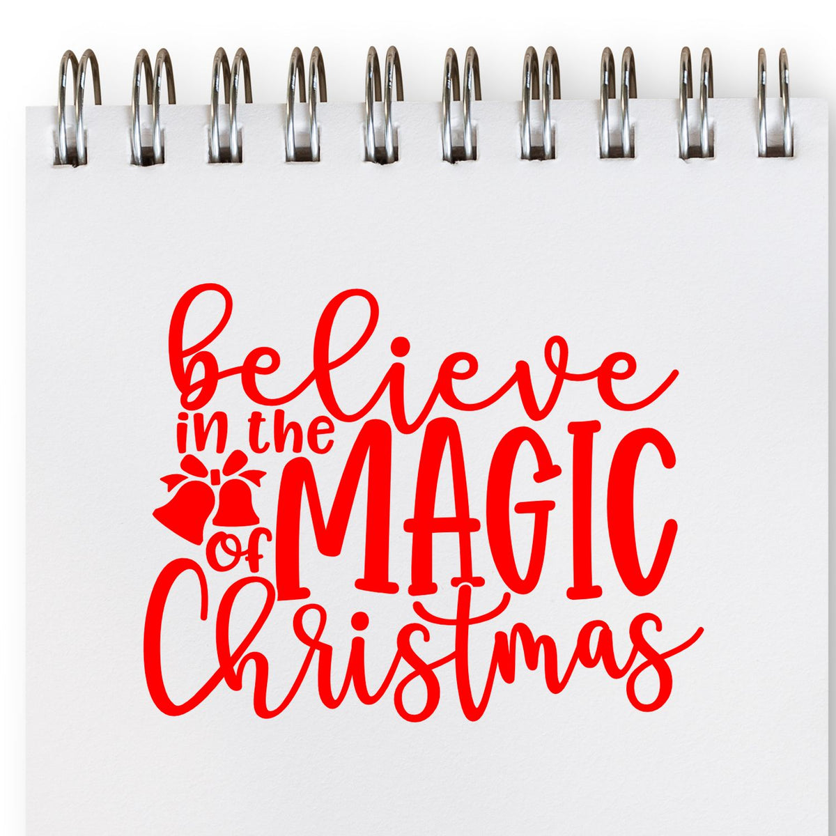 Holiday stamp and seal design in red on white spiral paper, reading believe in the magic of Christmas with bell icon.