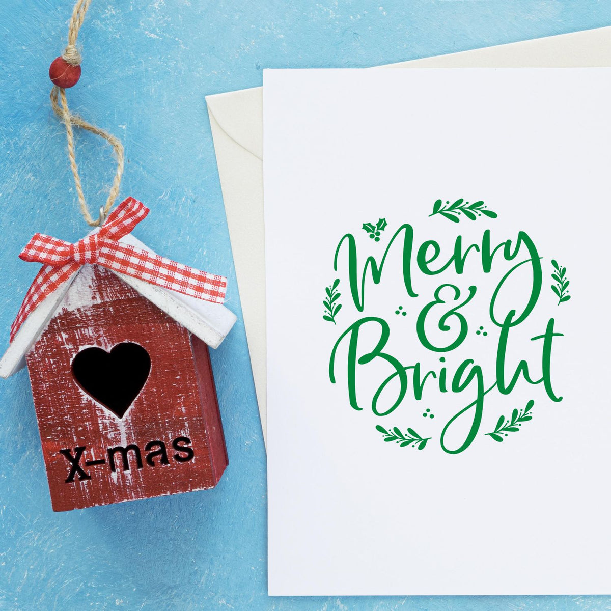 Rustic red wooden stamp-and-seal ornament with heart cutout beside a white card featuring a green Merry & Bright stamp on blue.