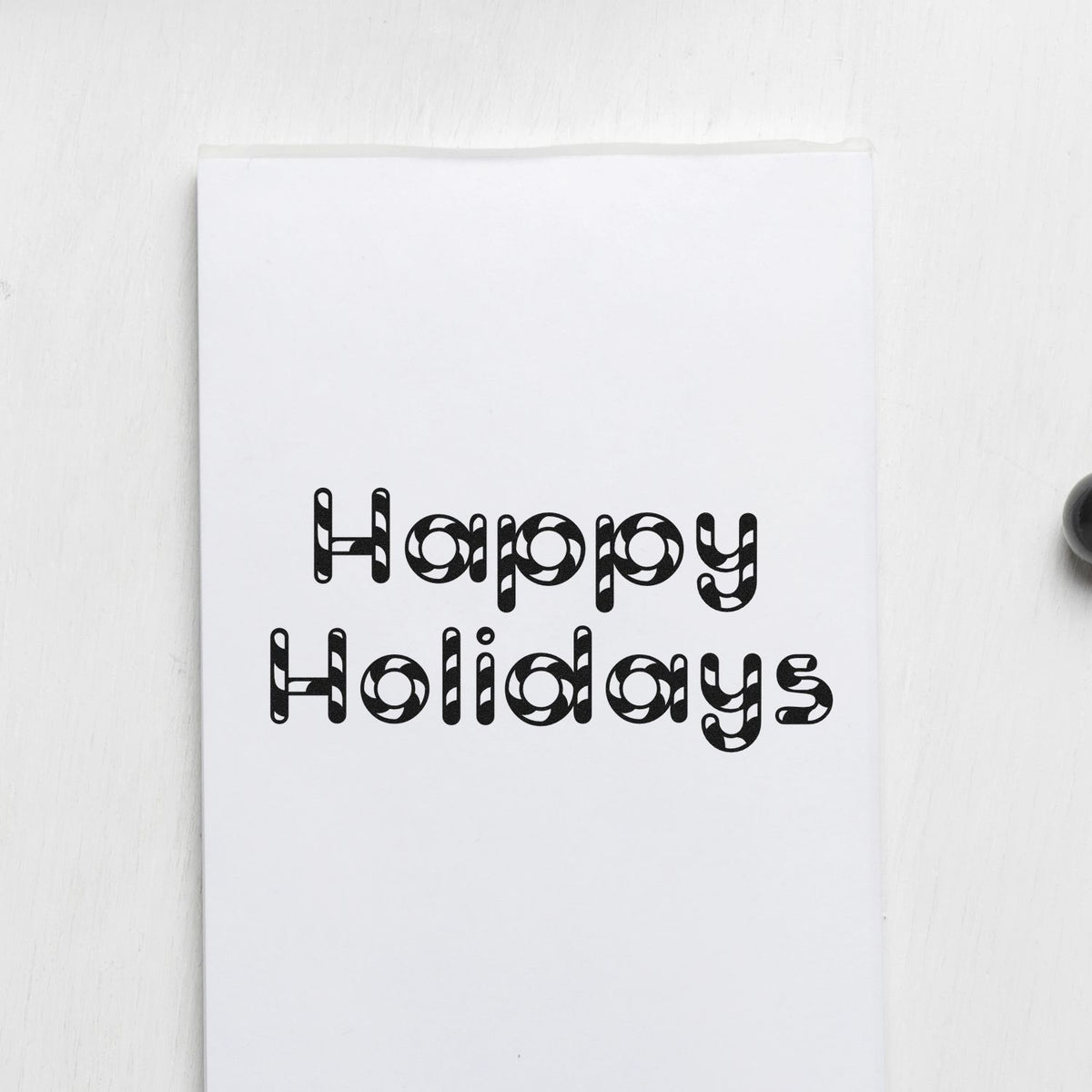 Black holiday stamp seal reading Happy Holidays on white paper.
