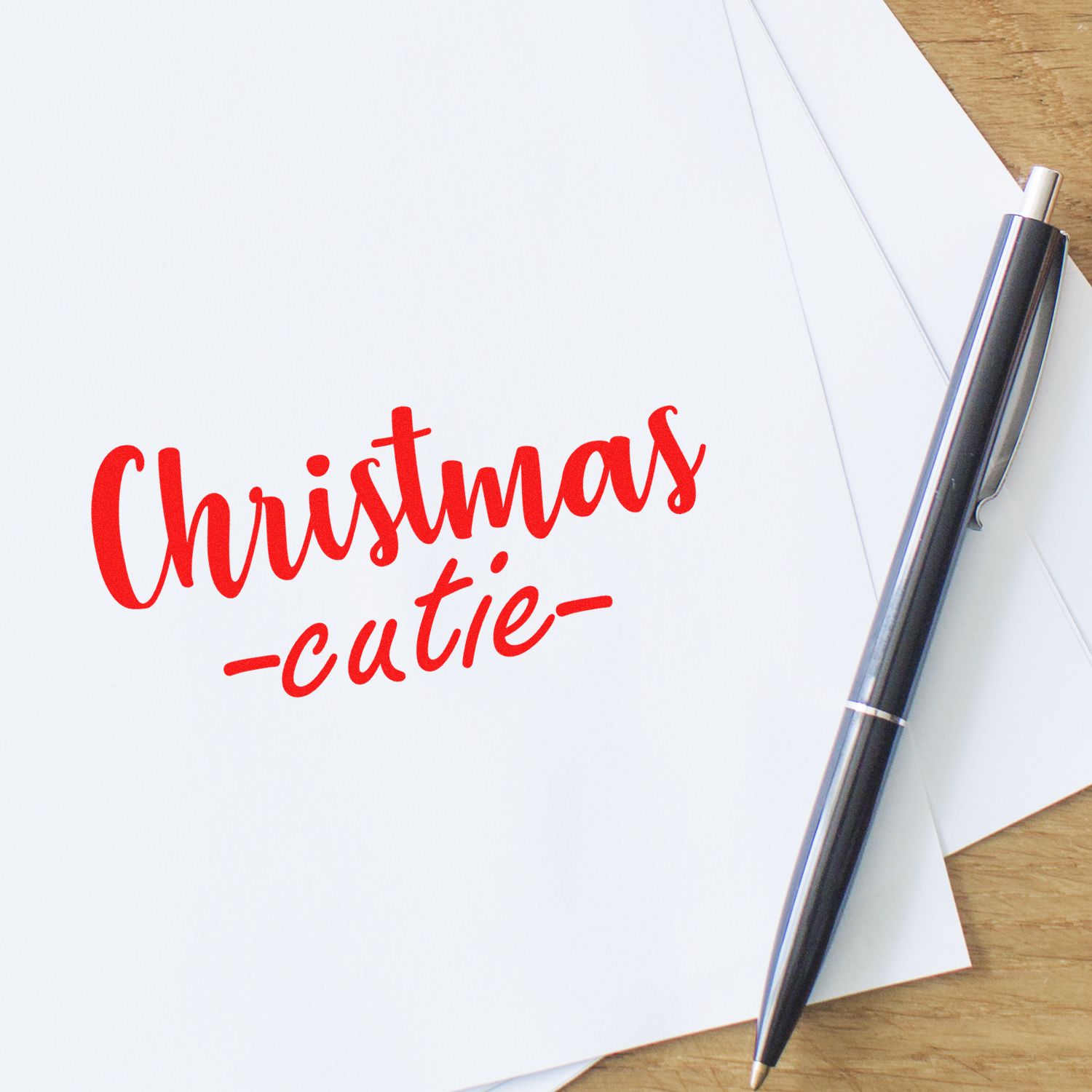 Red Christmas-cutie stamp and seal on white paper beside a black-silver pen on a wooden desk