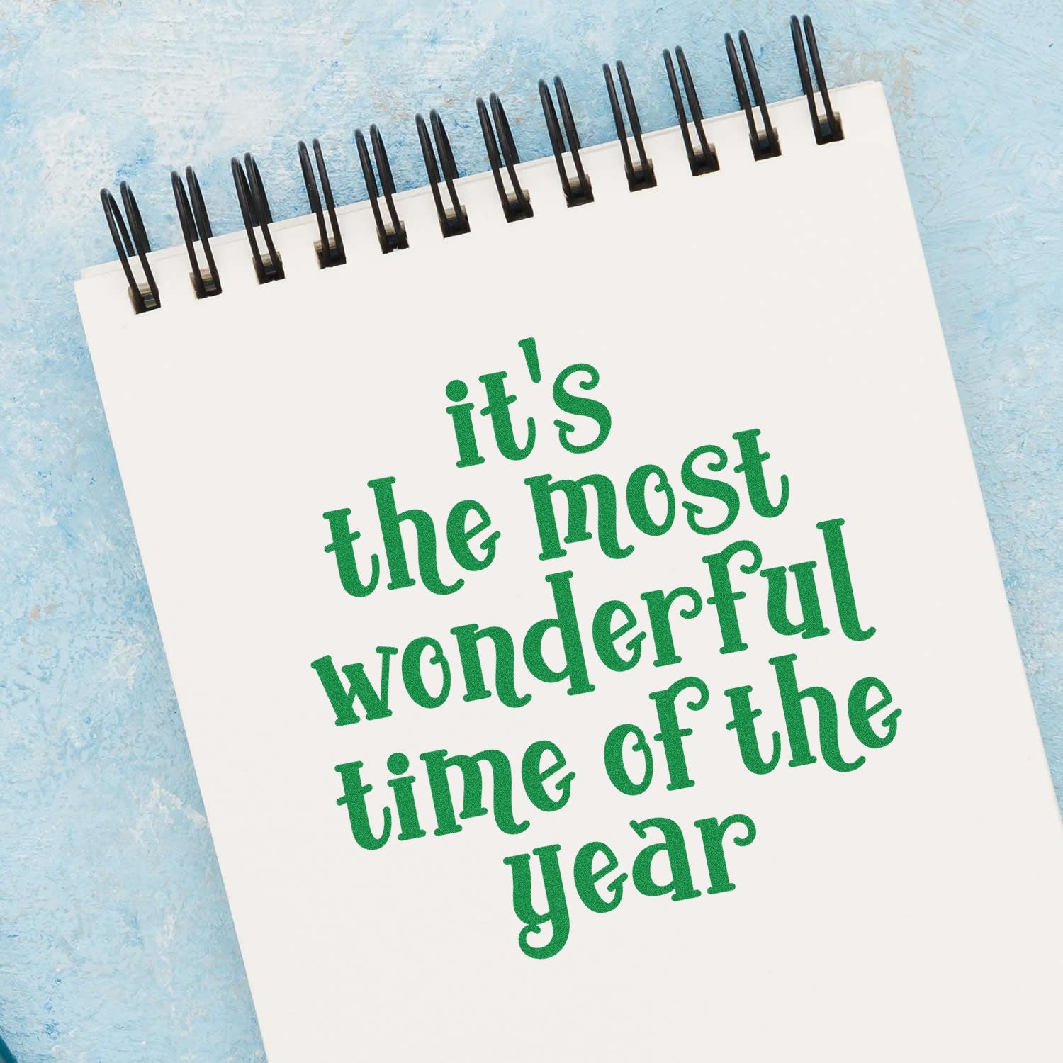White spiral notepad with green stamped its the most wonderful time of the year on a blue background, stamp and seal product.