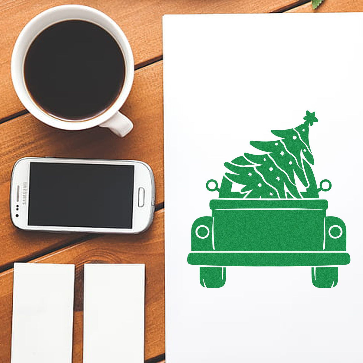 Green Christmas tree stamp and seal products on white paper beside a coffee cup and smartphone on a wooden desk.