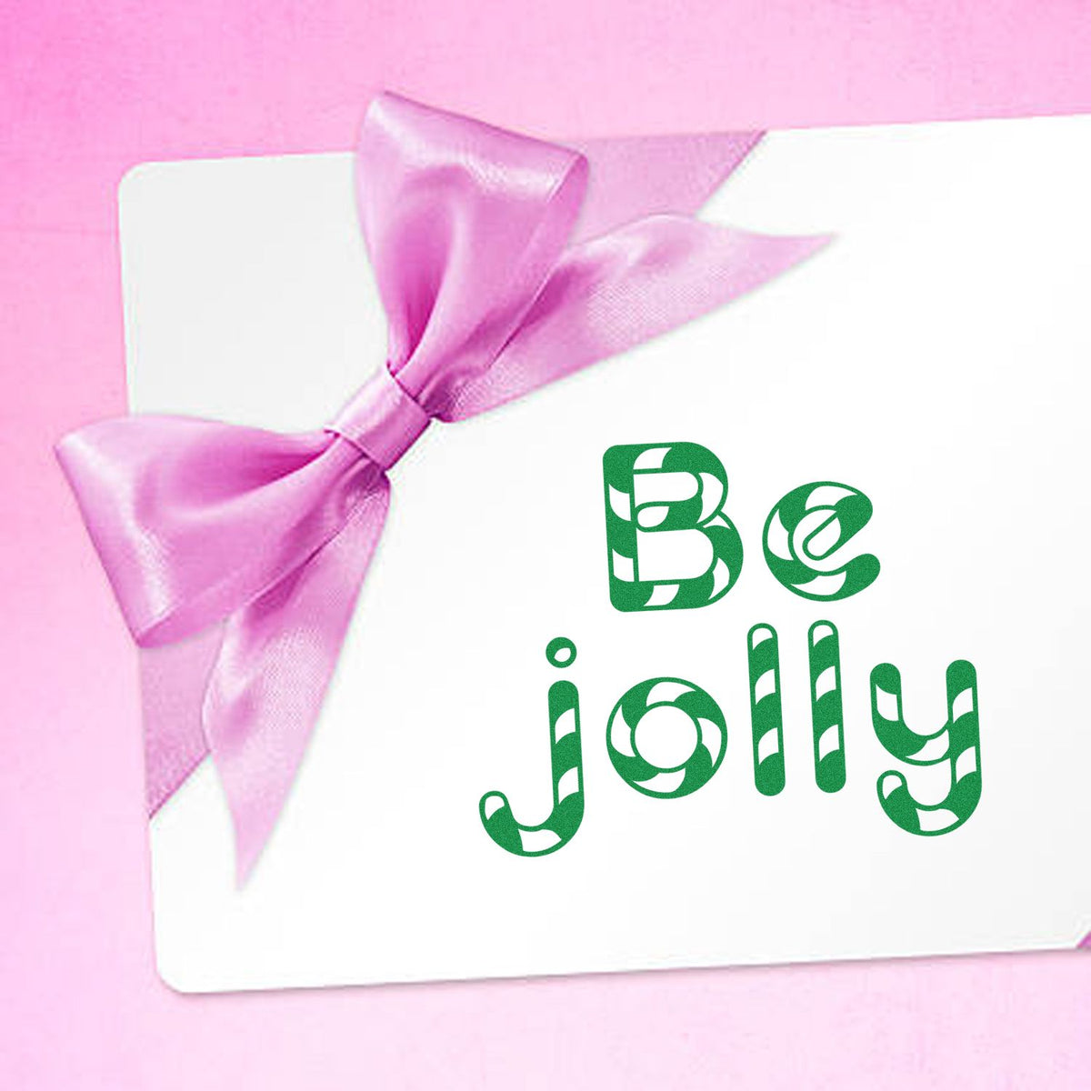 Pink satin bow on white card with green Be jolly holiday stamp and seal design