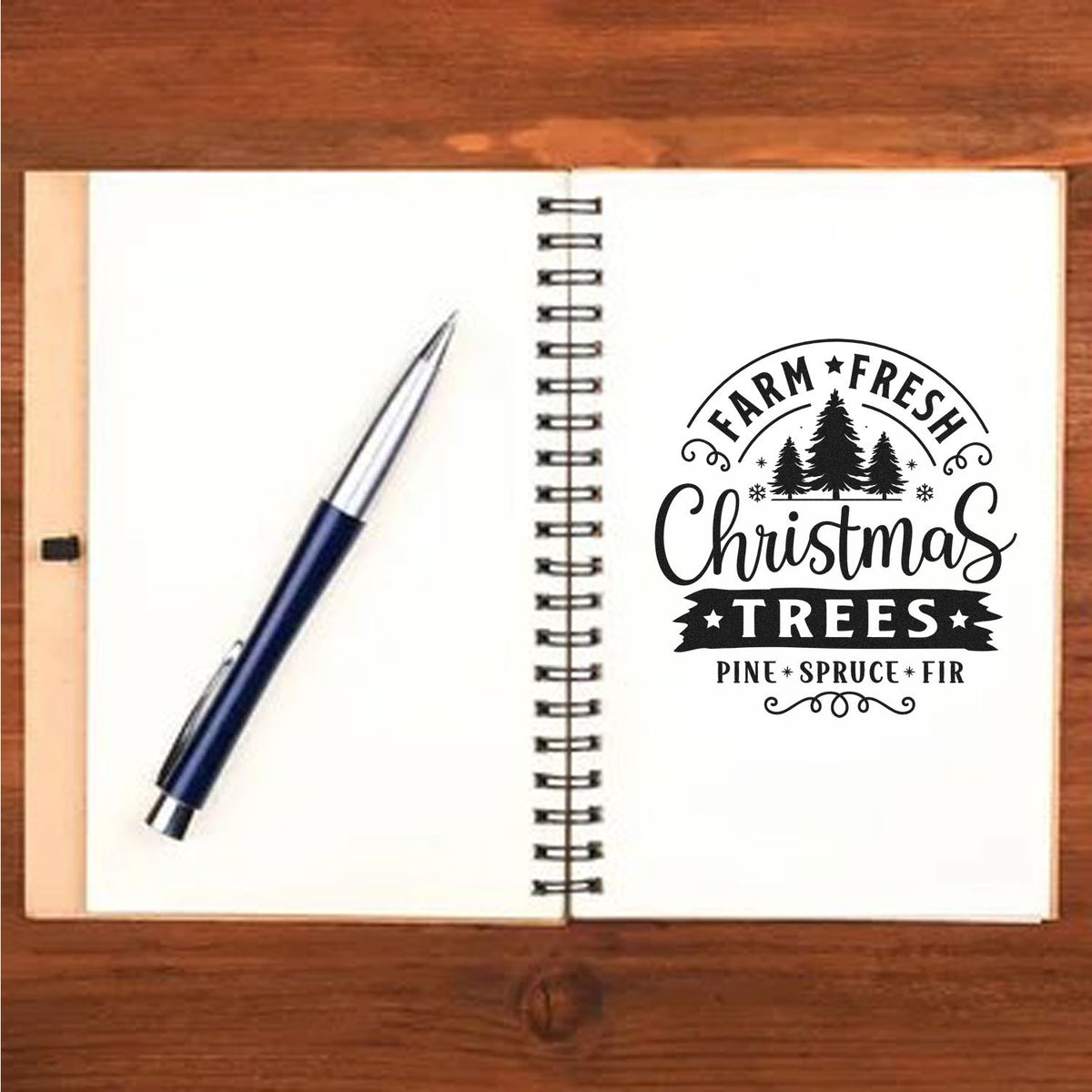 Open spiral notebook on wood with blue pen and black Farm Fresh Christmas Trees stamp seal.