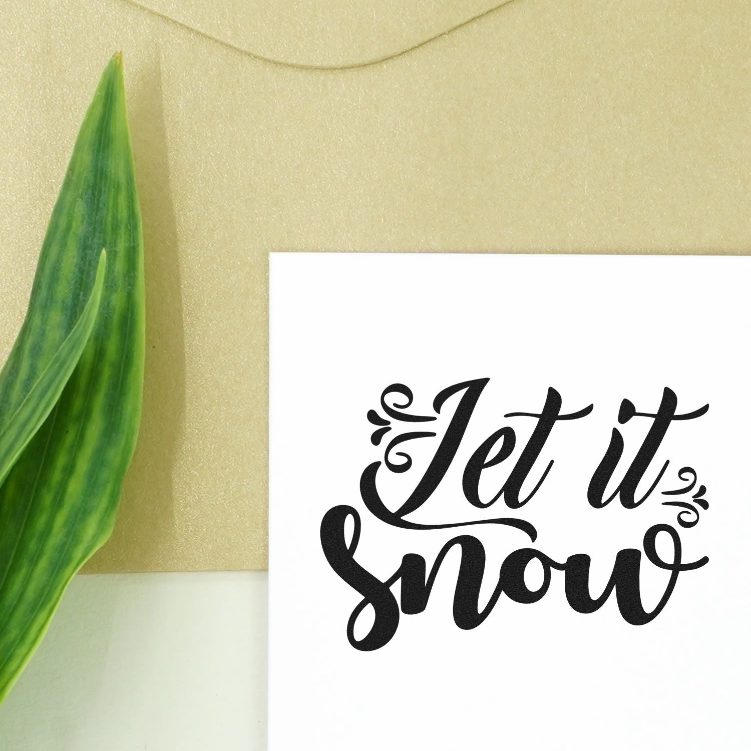 Black Let it Snow stamp and seal on a white card, with a green leaf accent and beige background.