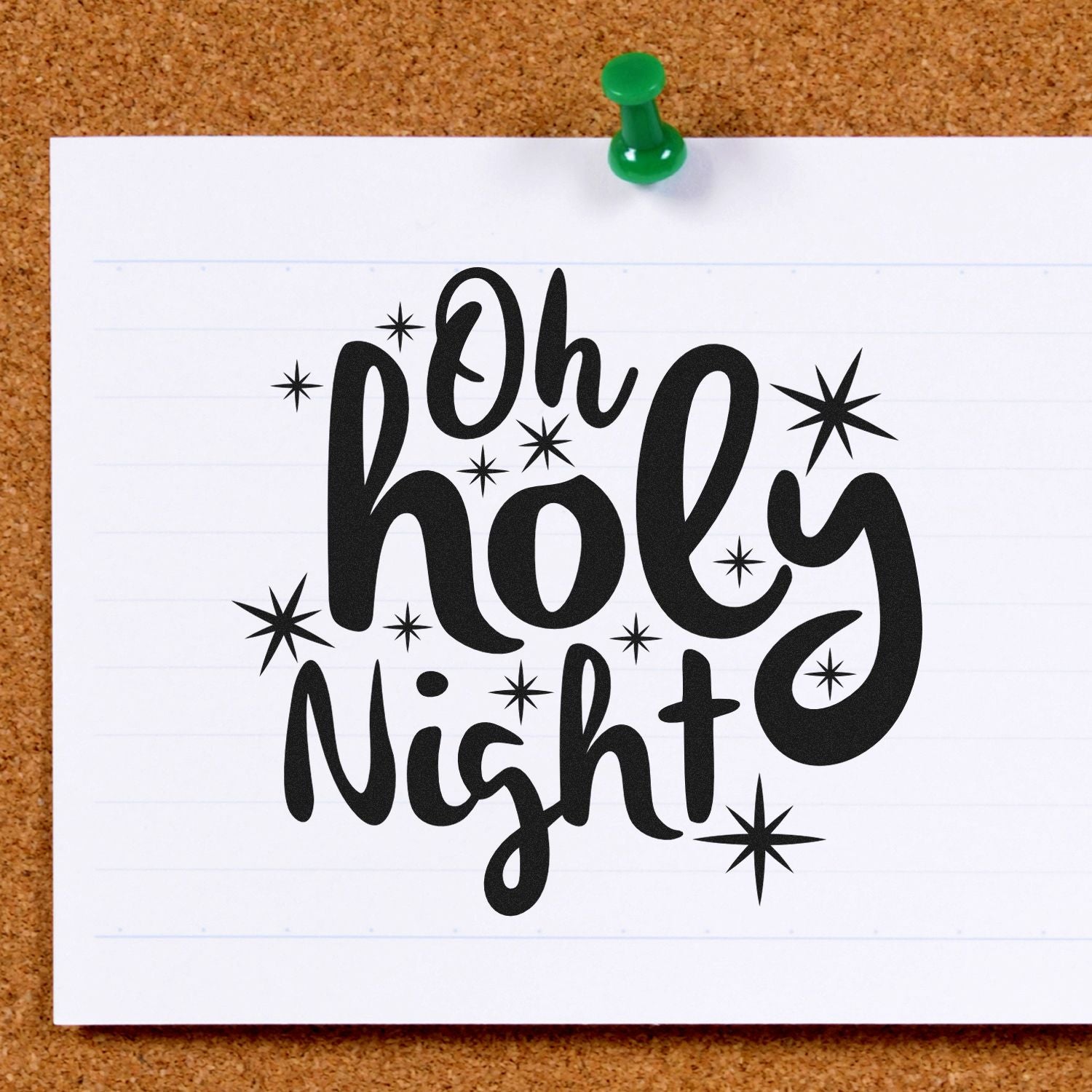 Black Oh Holy Night stamp and seal design with starbursts on white paper, pinned to a corkboard with a green pushpin.
