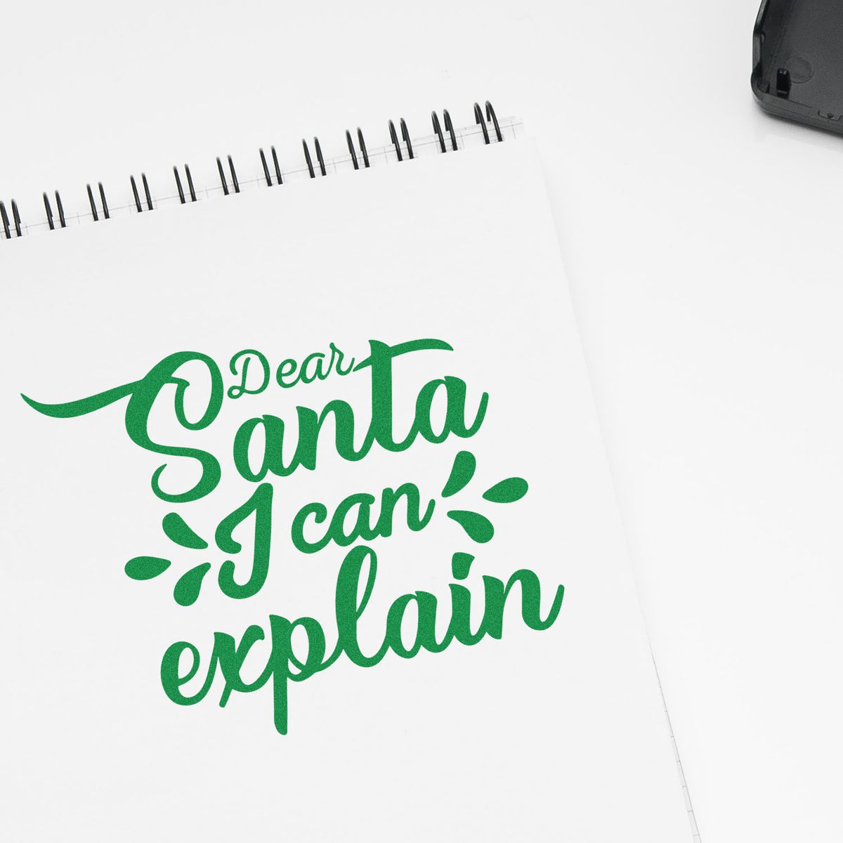 Green custom stamp and seal design reading Dear Santa I can explain on a white spiral notebook.
