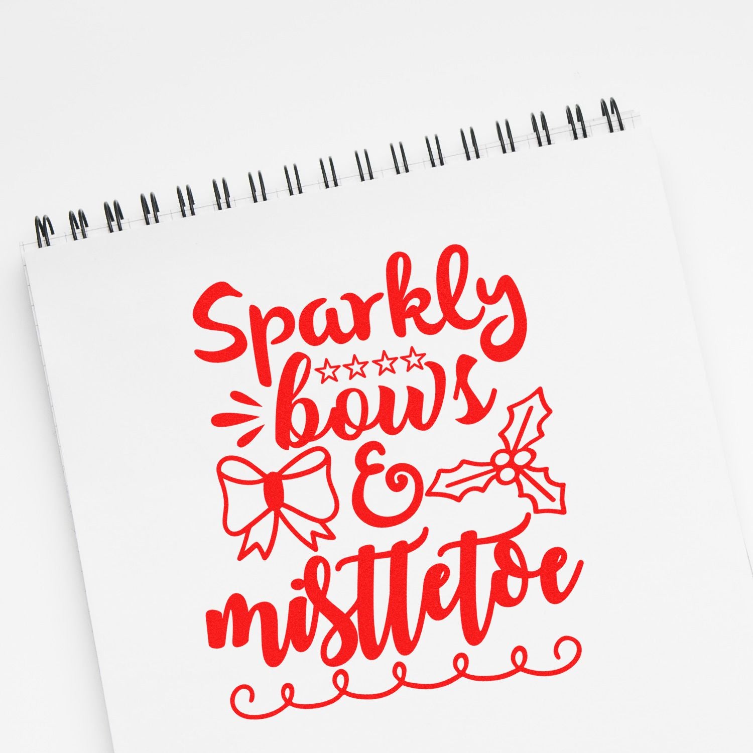 Red holiday stamp-and-seal design reading Sparkly bows & mistletoe, with bow, holly, stars on a white spiral notebook.