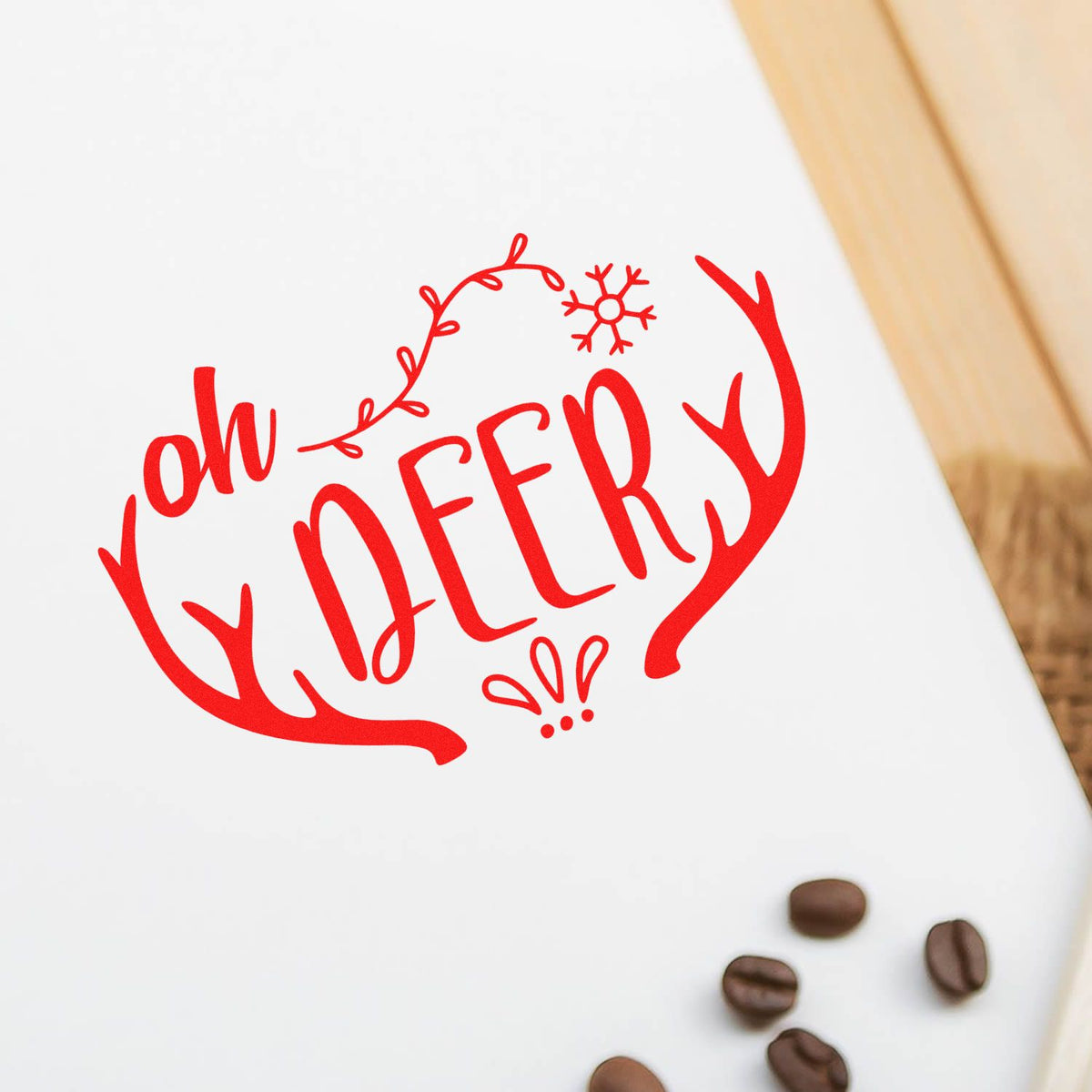 Red oh DEER! festive stamp/seal with antlers and snowflake on white paper, accented by coffee beans.
