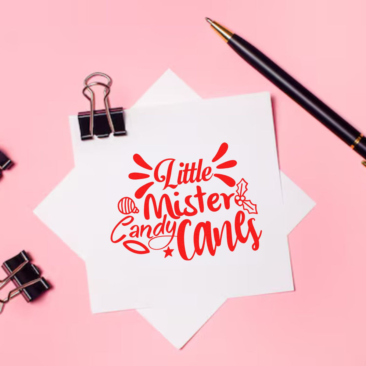 Red holiday stamp and seal design reading "Little Mister Candy Canes" on white paper, with pink background, binder clip, and pen.