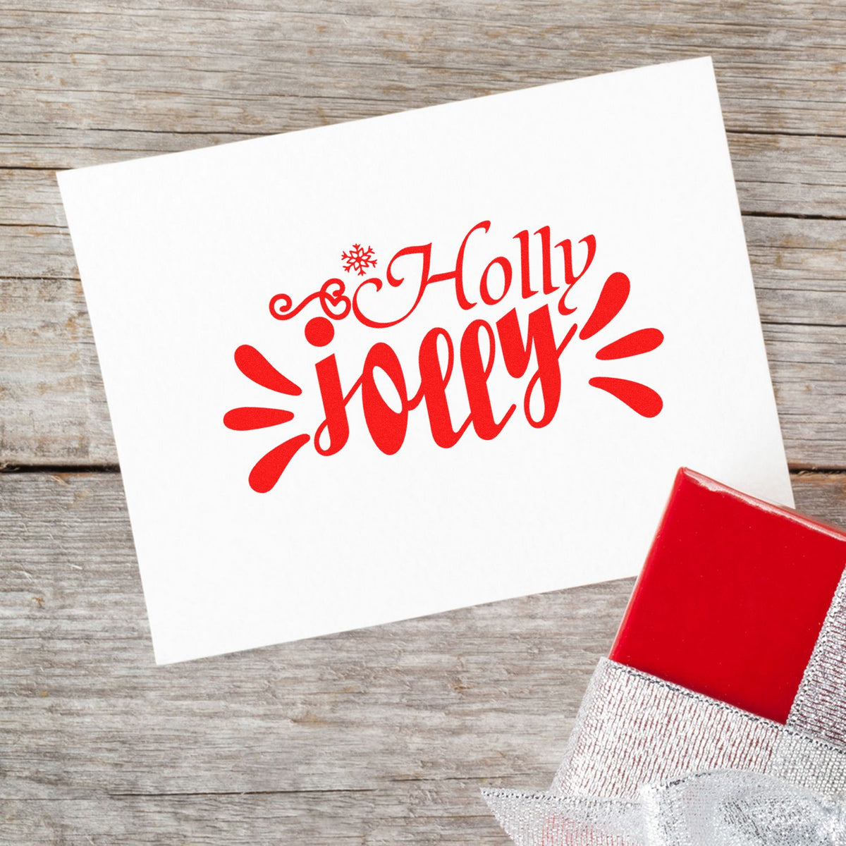 Red holiday stamp and seal with Holly jolly on a white card, beside a red gift box.