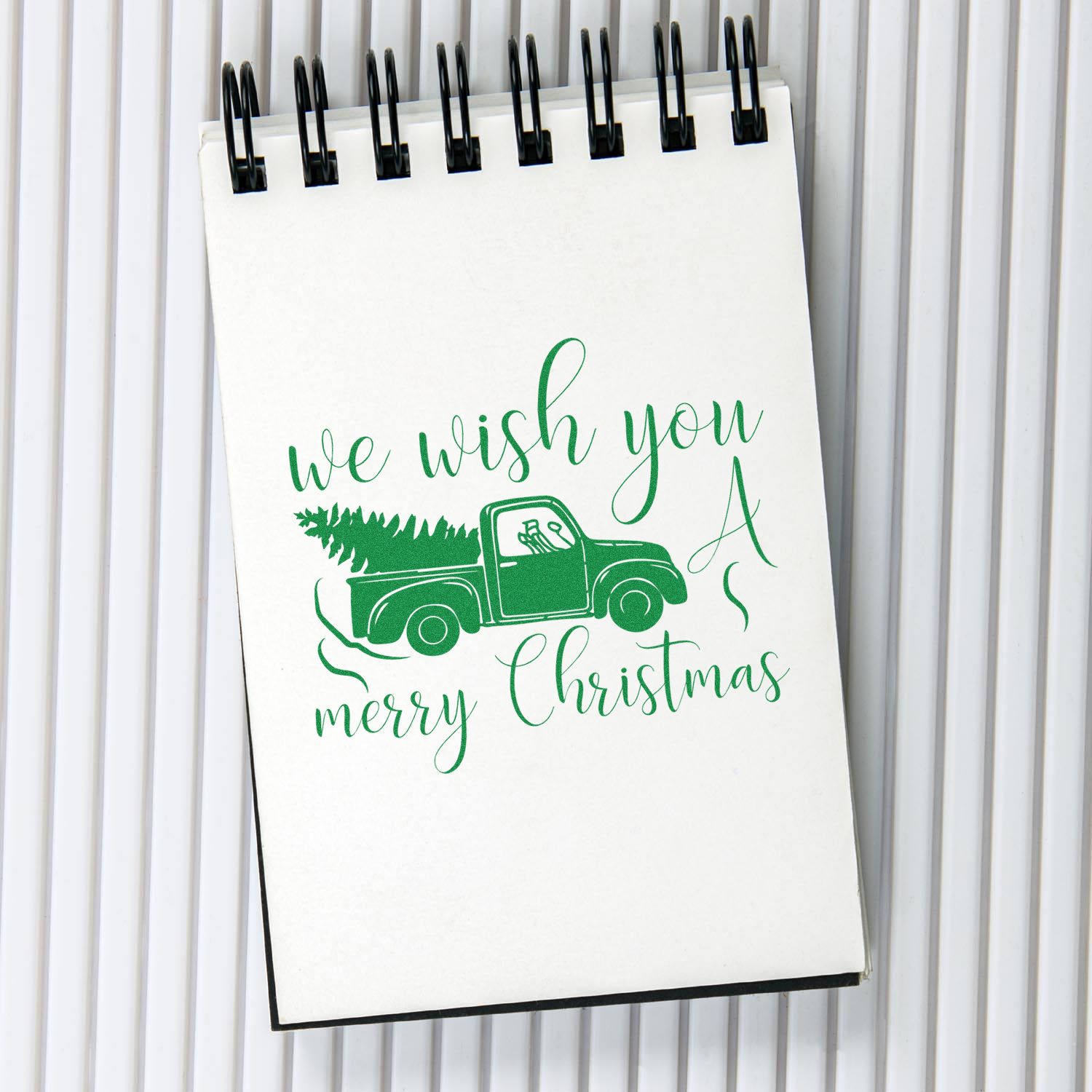 Green Merry Christmas stamp/seal with vintage truck carrying a tree on a white spiral notebook.