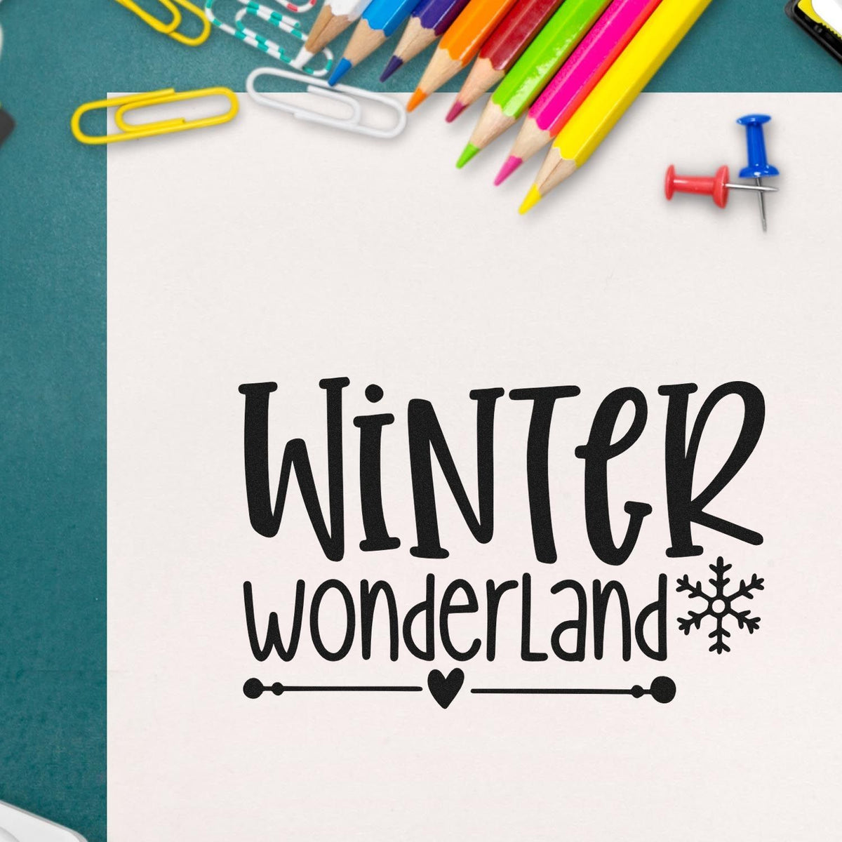 Winter Wonderland stamp and seal design in black with snowflake and heart, surrounded by colorful pencils and push pins.
