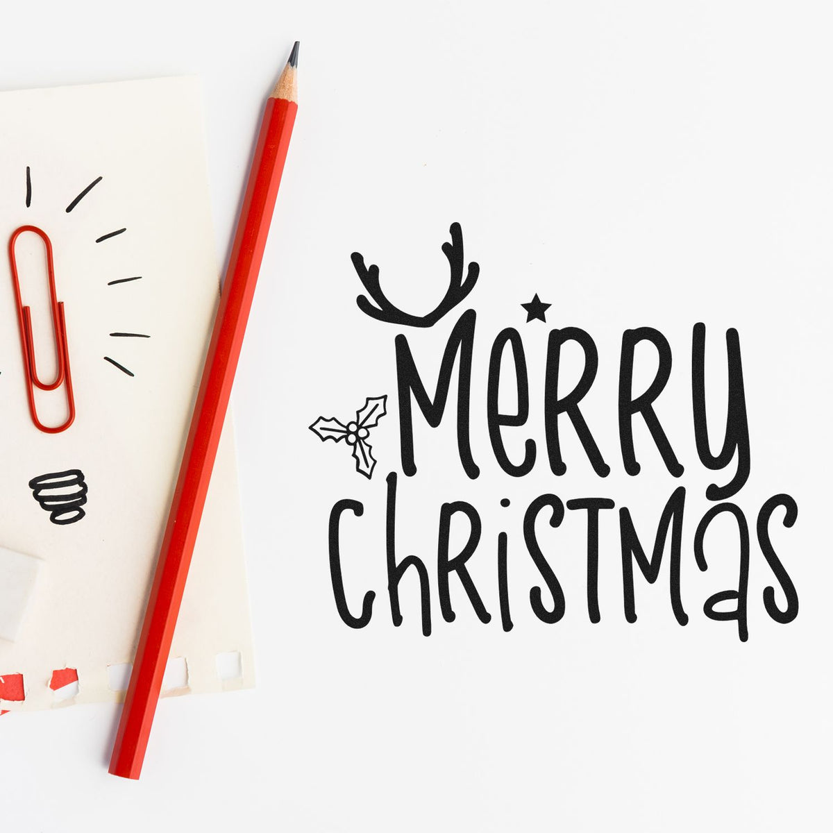 Holiday stamp and seal sample with black Merry Christmas text, holly and antlers on white paper, plus a red pencil.