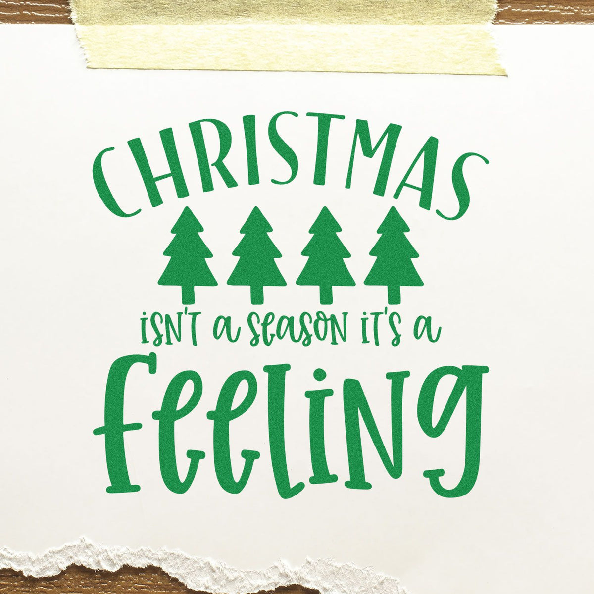 Green Christmas sentiment stamp and seal design with four pine trees on white paper, taped top and torn bottom.