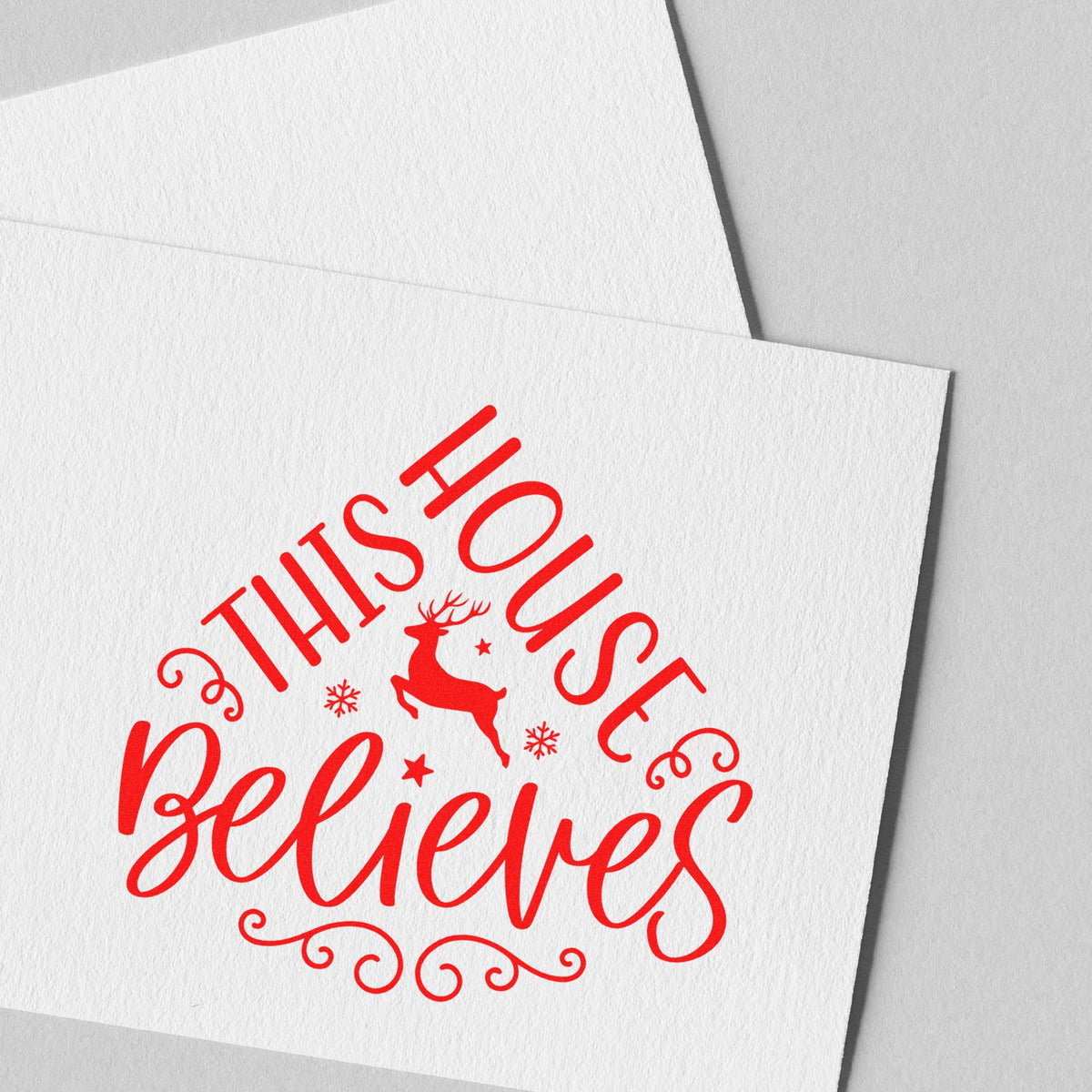 Red holiday stamp and seal design reading This House Believes with reindeer, snowflakes, and swirls on white paper.