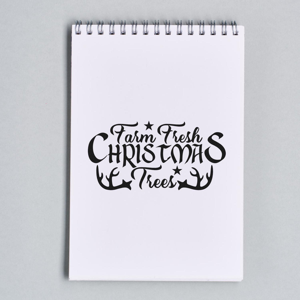 Black Farm Fresh Christmas Trees stamp/seal design on white spiral notebook, with stars and antlers.