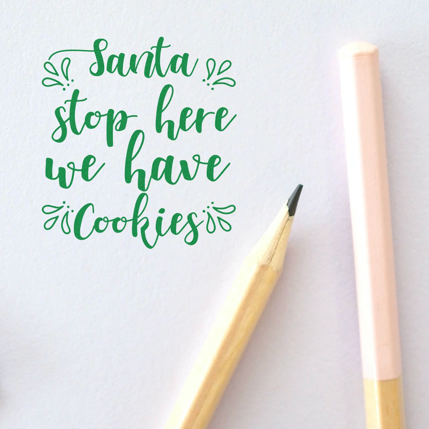 Green custom stamp and seal with Santa stop here we have cookies, decorative flourishes, beside a pencil on white paper.