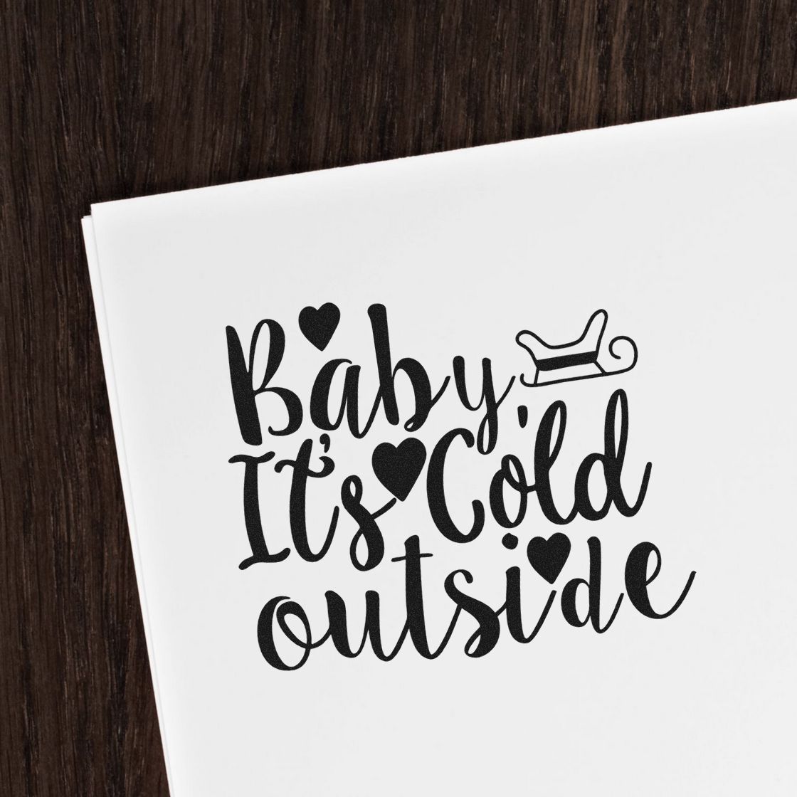 Black stamp and seal design on white paper reading Baby Its Cold Outside with hearts and a sleigh icon.