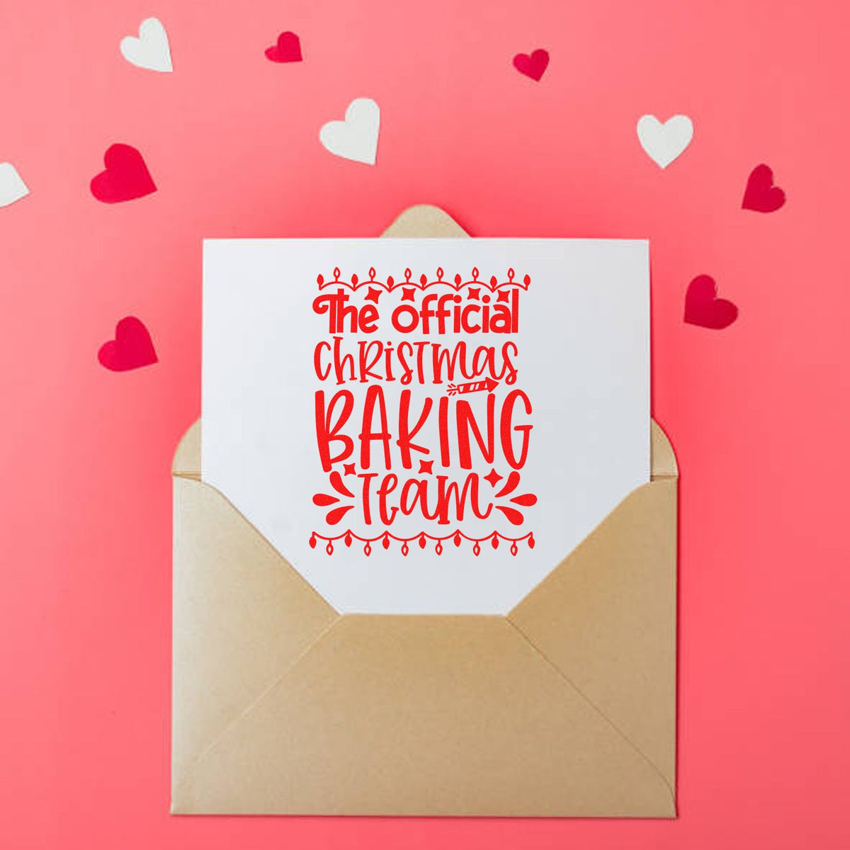 Red Christmas baking team stamp seal on white card in tan envelope, against a pink background with red and white hearts.