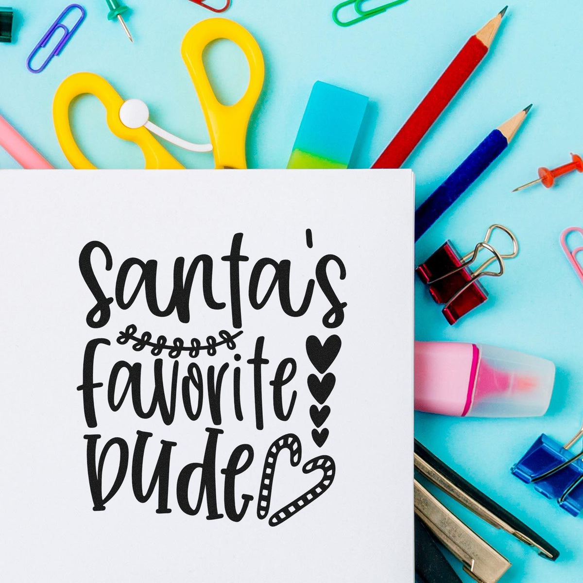Black Santas favorite dude stamp design on white card, with colorful stamp and seal supplies on a turquoise background.