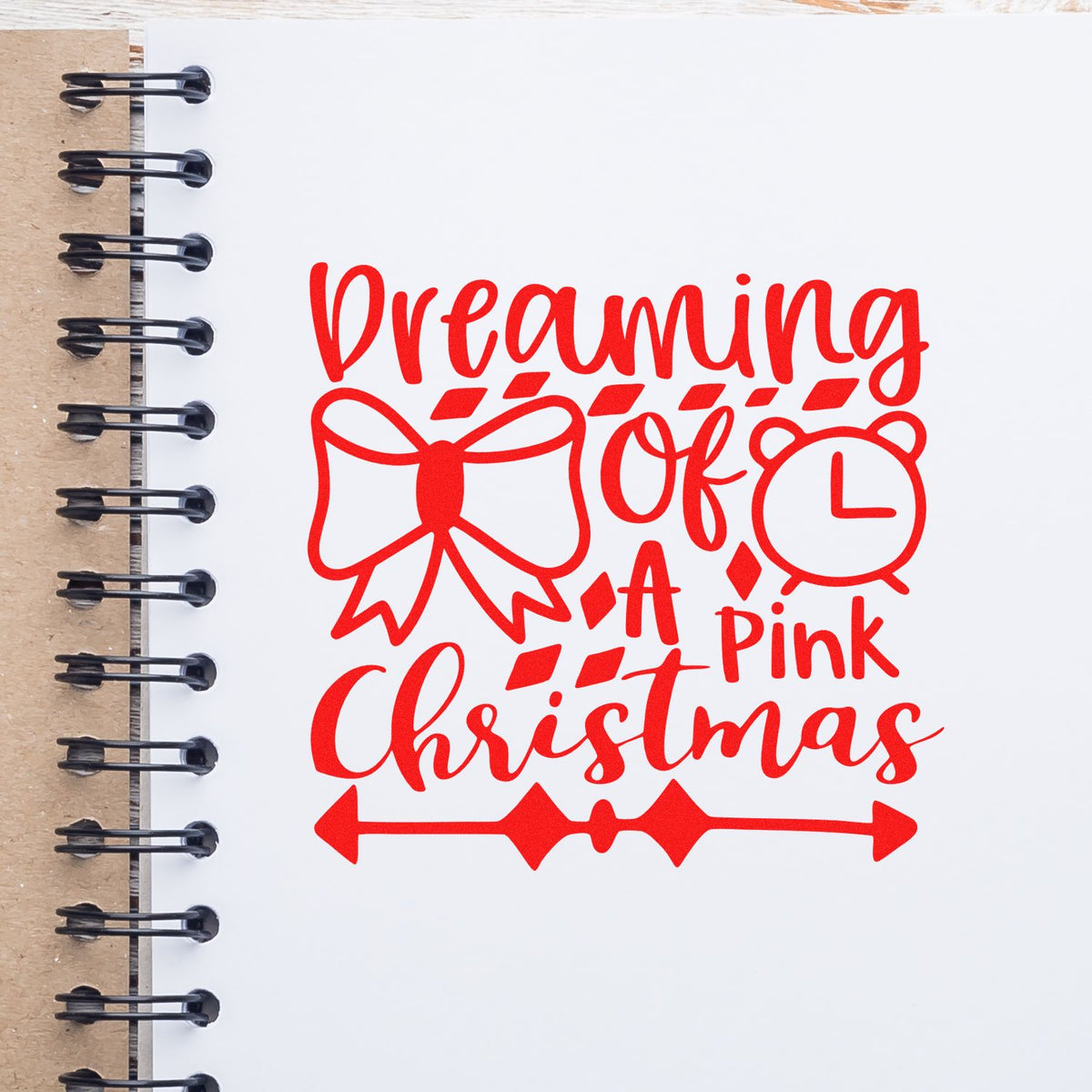 Red holiday stamp seal reading Dreaming of a Pink Christmas, with bow, alarm clock, and arrows on white paper.