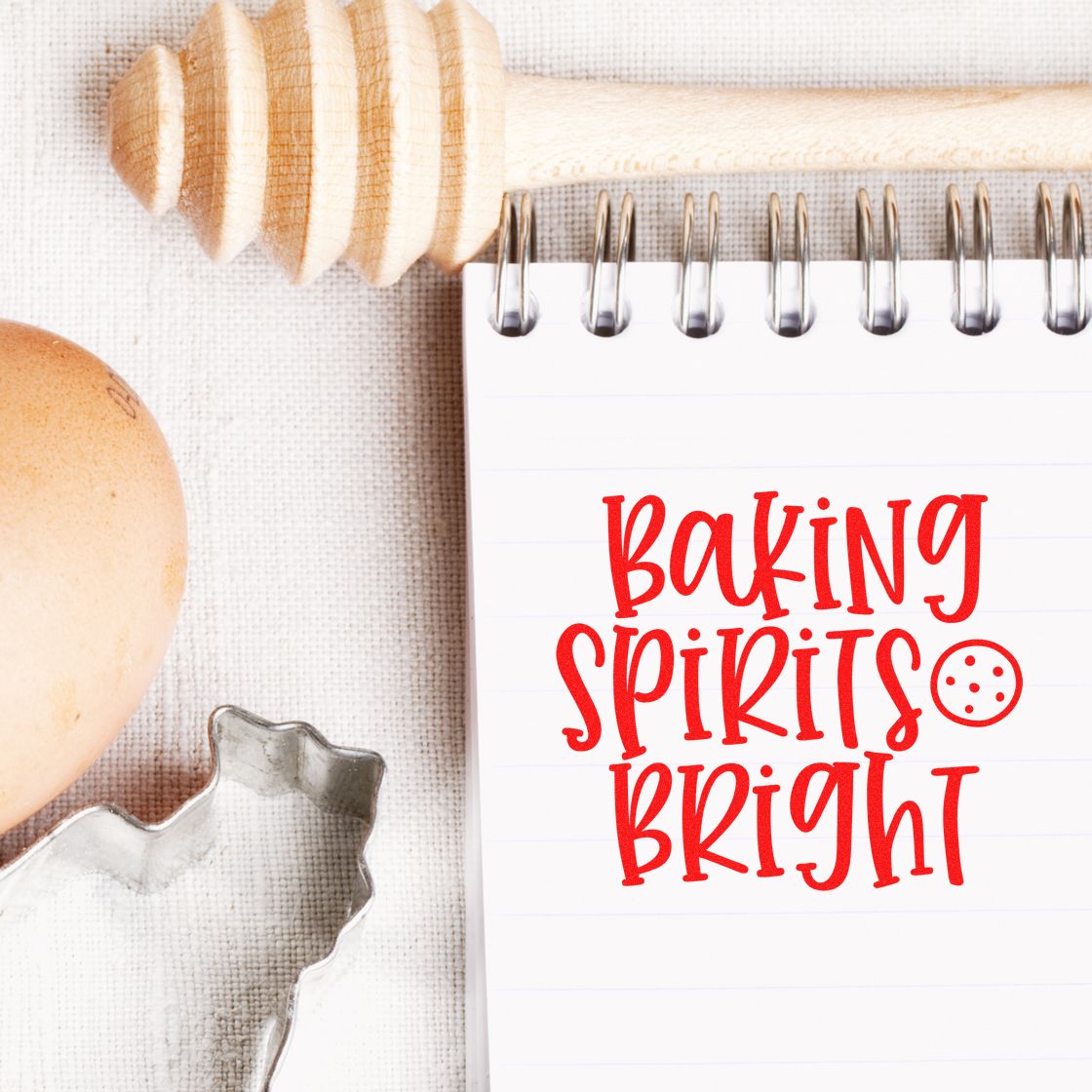 Baking Spirits Bright red stamp/seal design on spiral notebook with wooden honey dipper, egg, and cookie cutter.