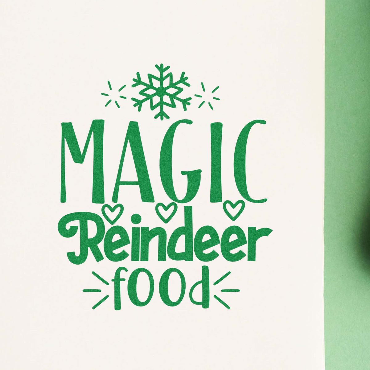 Green festive stamp seal reading Magic Reindeer Food with snowflake and heart accents on white paper.