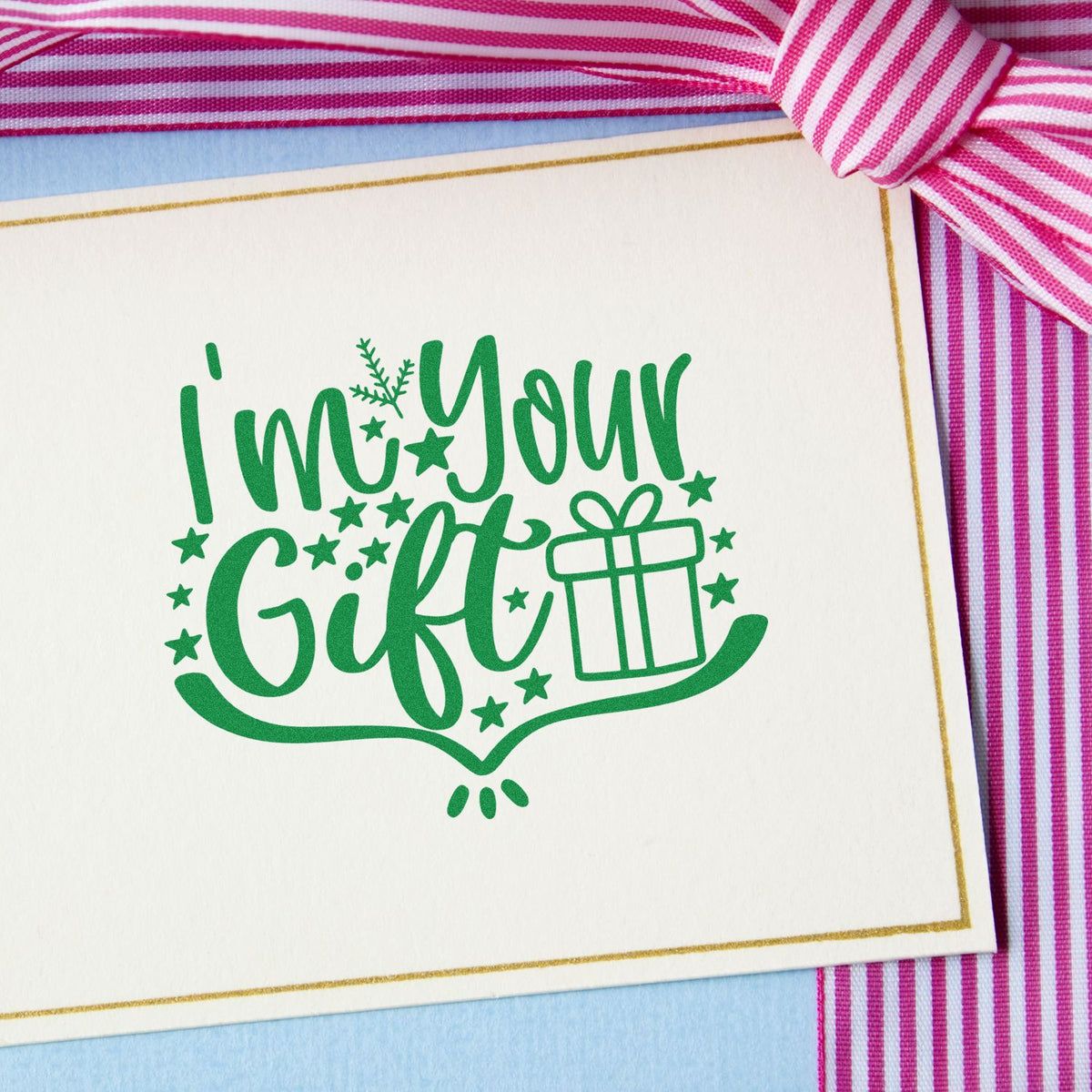 Green Im Your Gift stamp seal on cream card with gold border, pink striped ribbon, and gift icon