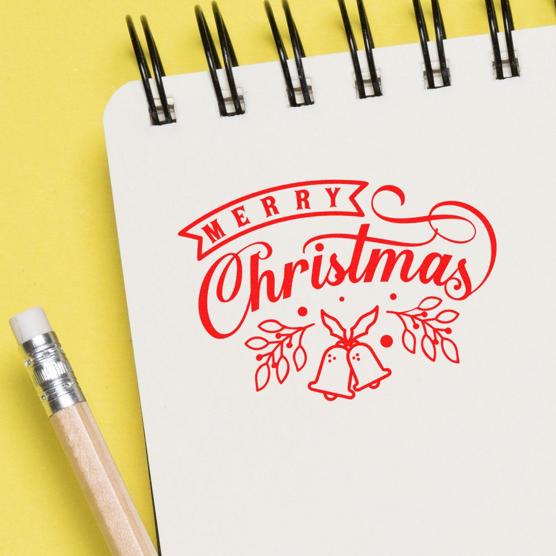 Red Merry Christmas stamp and seal with bells and holly on a white notebook over a yellow background.