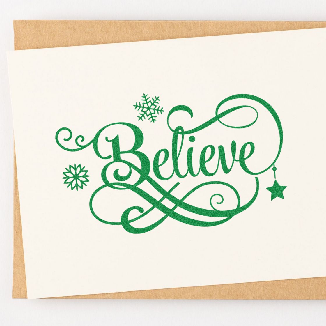 Green decorative Believe holiday stamp and seal design with snowflakes and hanging star on cream card.