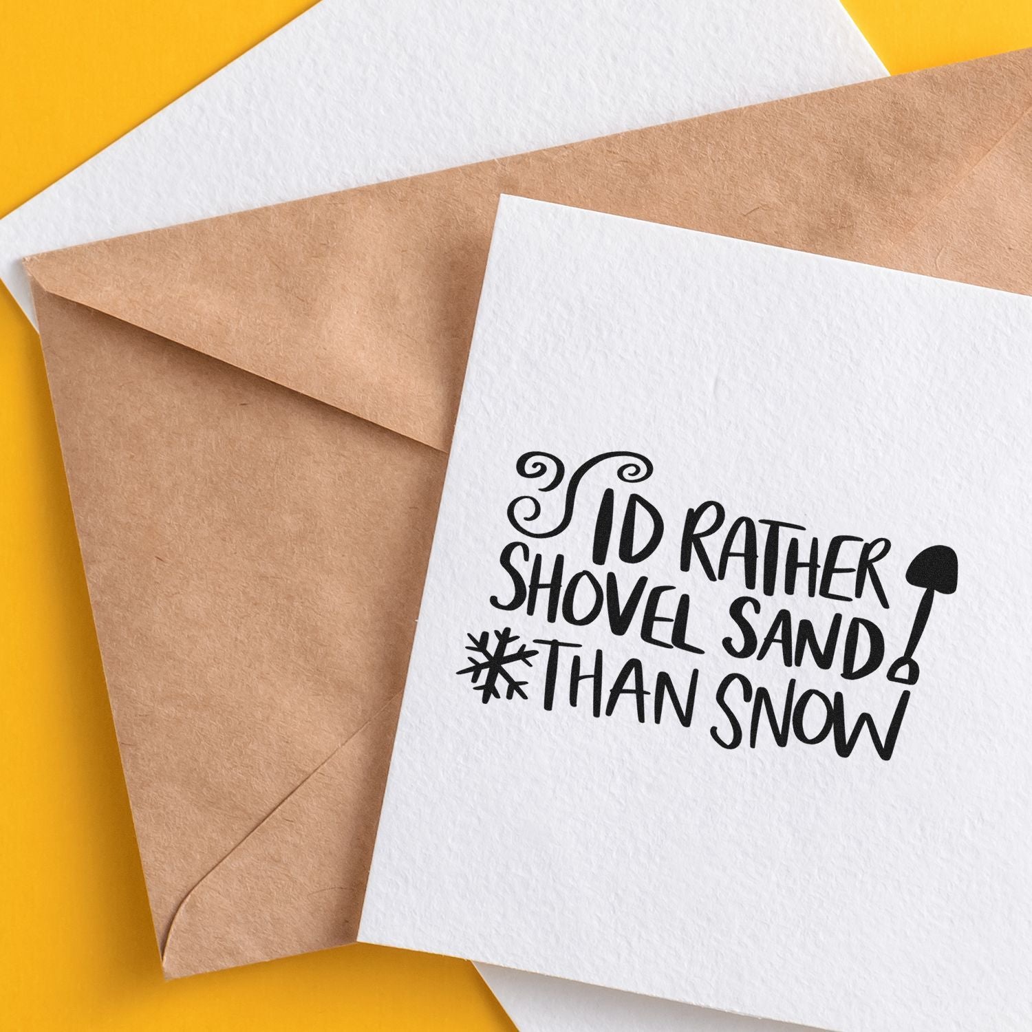 Custom stamp and seal card with black Id rather shovel sand than snow text, layered on kraft envelopes over yellow.