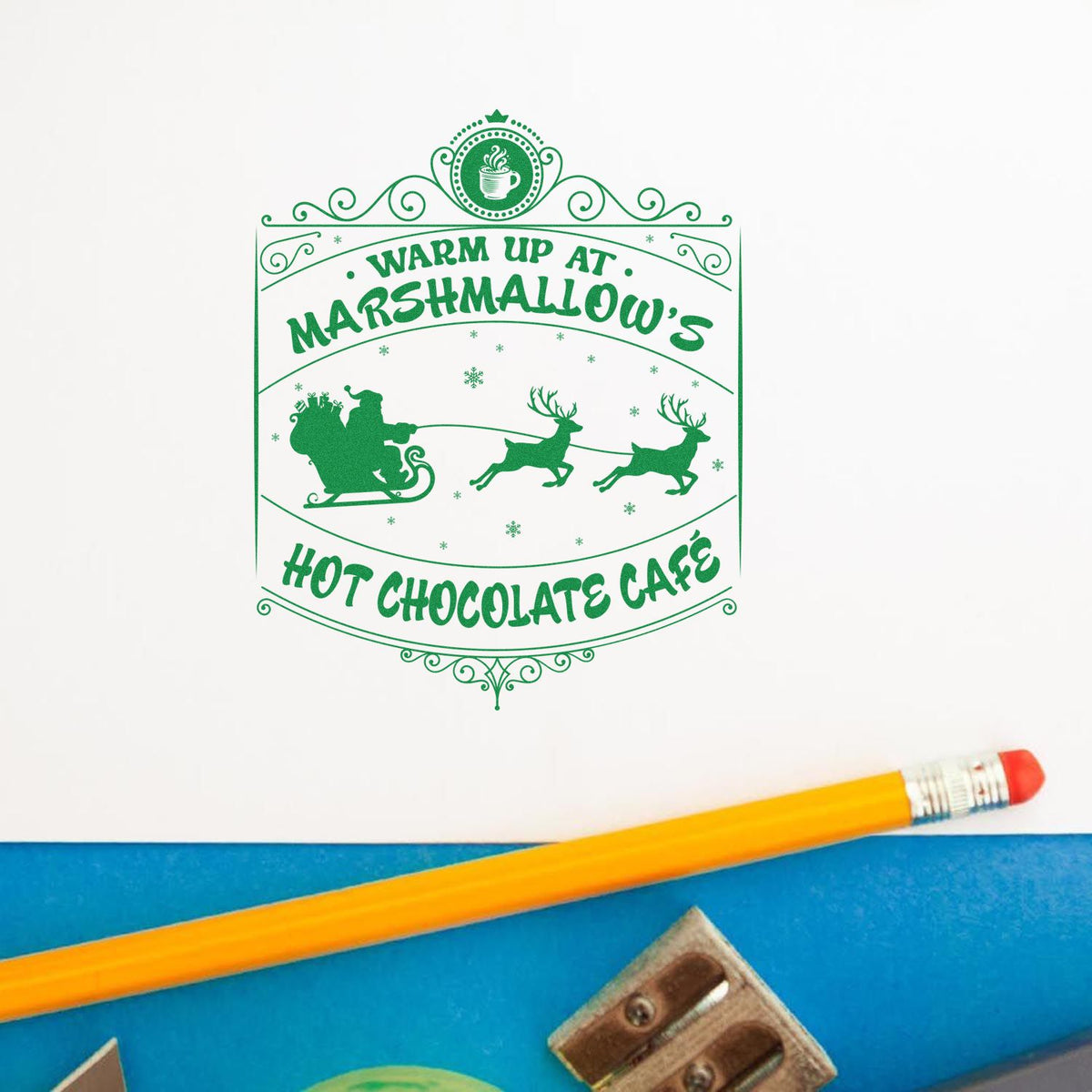 Green holiday stamp seal reading Warm Up at Marshmallows Hot Chocolate Cafe, with Santa sleigh, reindeer and snowflakes.