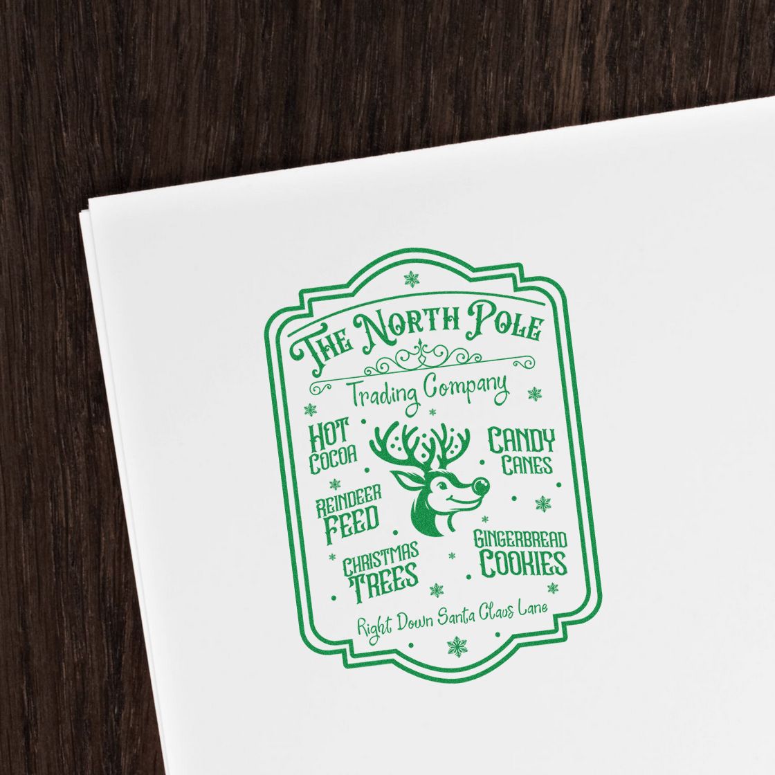 Green vintage Christmas stamp and seal for The North Pole Trading Company with reindeer, candy canes, cocoa and cookies on white paper.