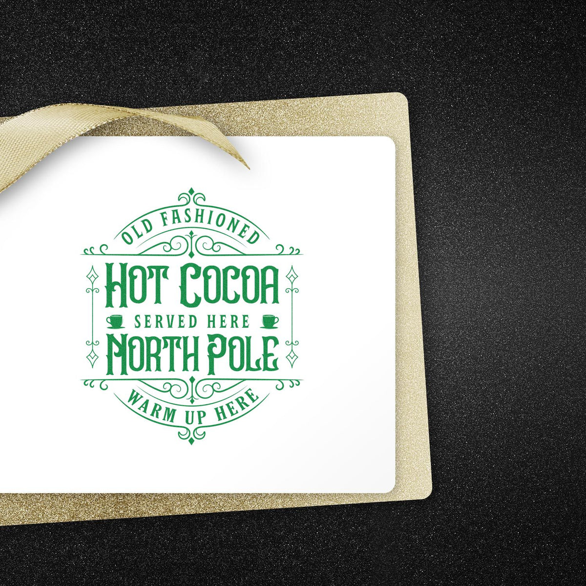 Green vintage hot cocoa North Pole stamp on white card with gold ribbon and glittery gold border against black background