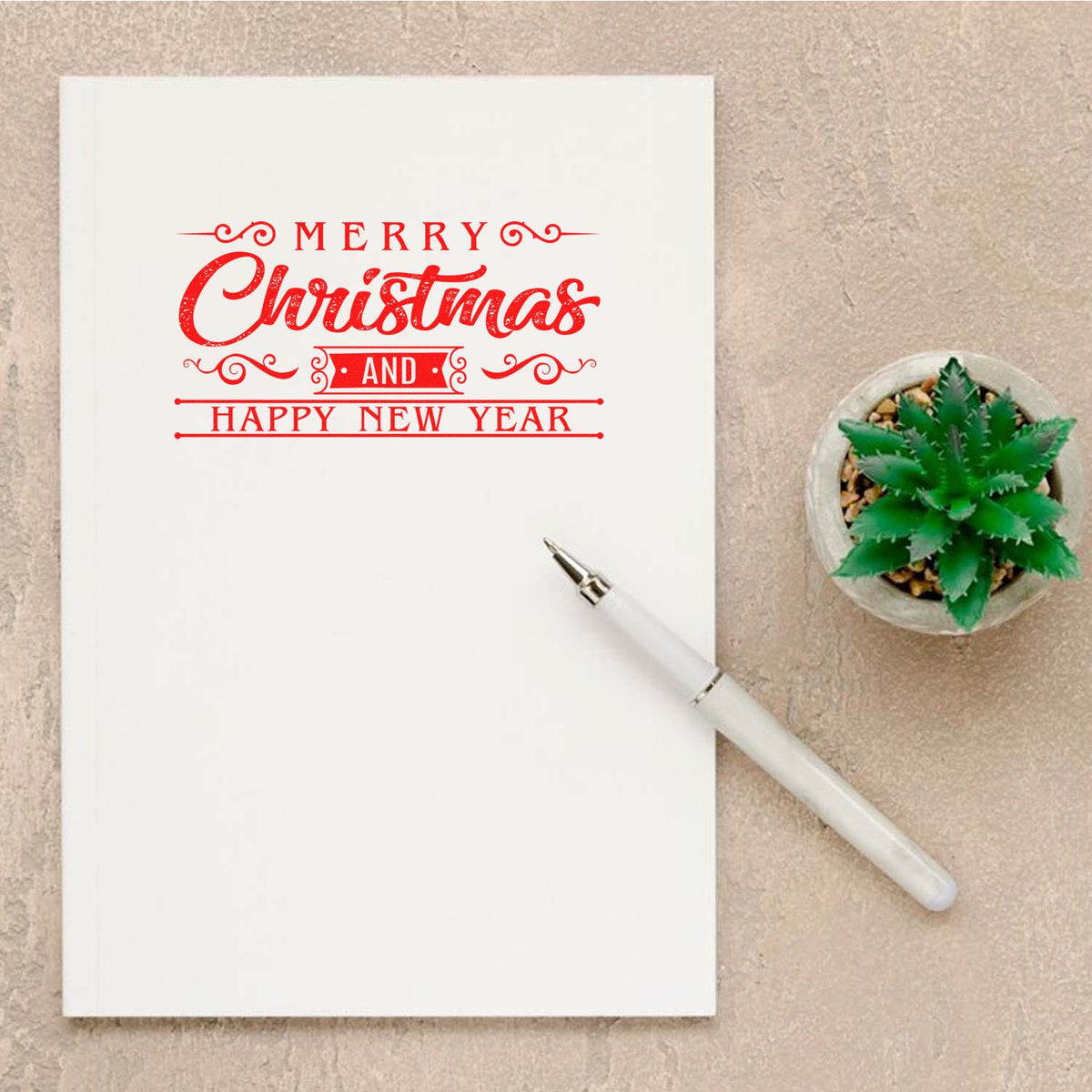 Red Merry Christmas and Happy New Year stamp seal on white card, with white pen and green succulent.