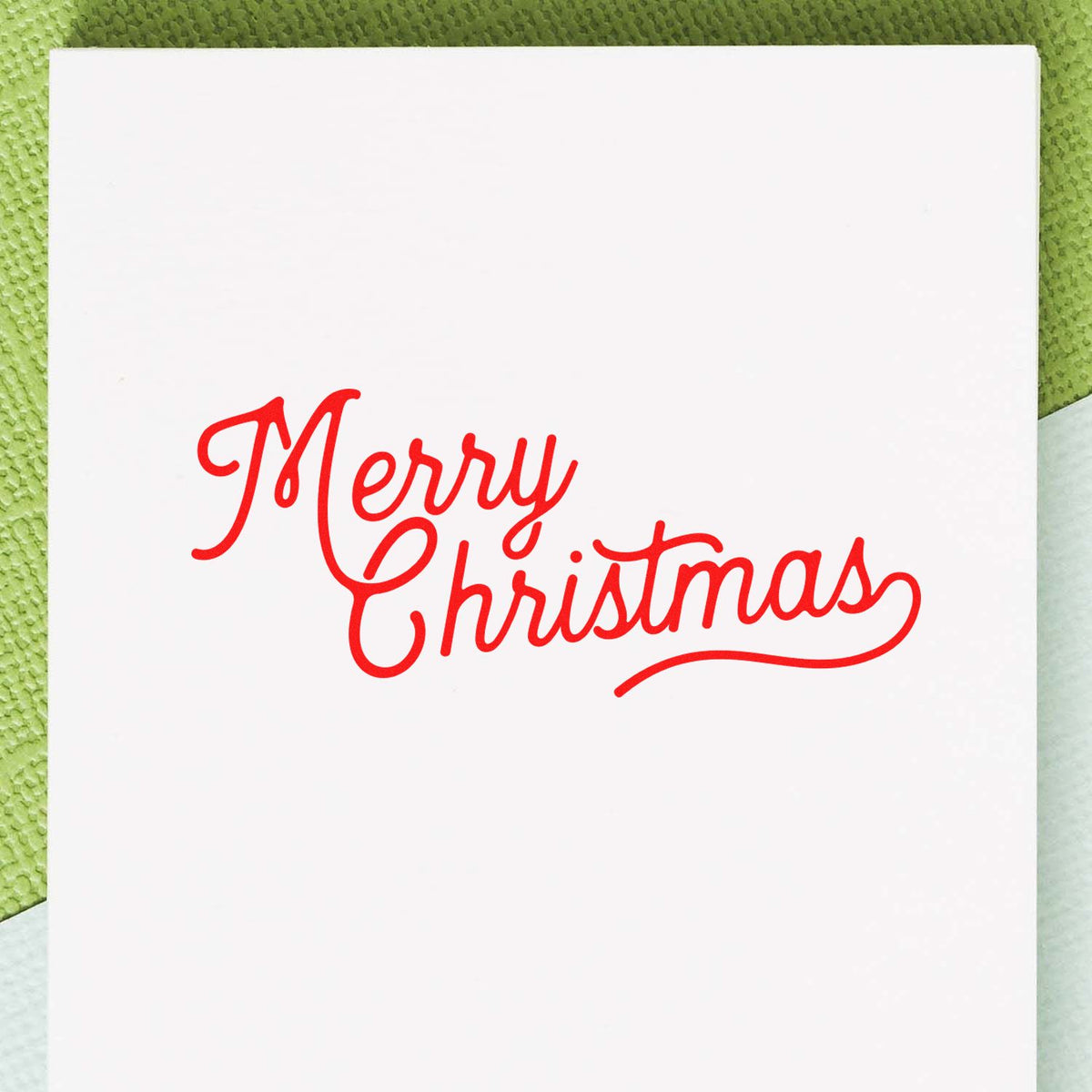 Red Merry Christmas stamp/seal in decorative script on a white card with green textured background.