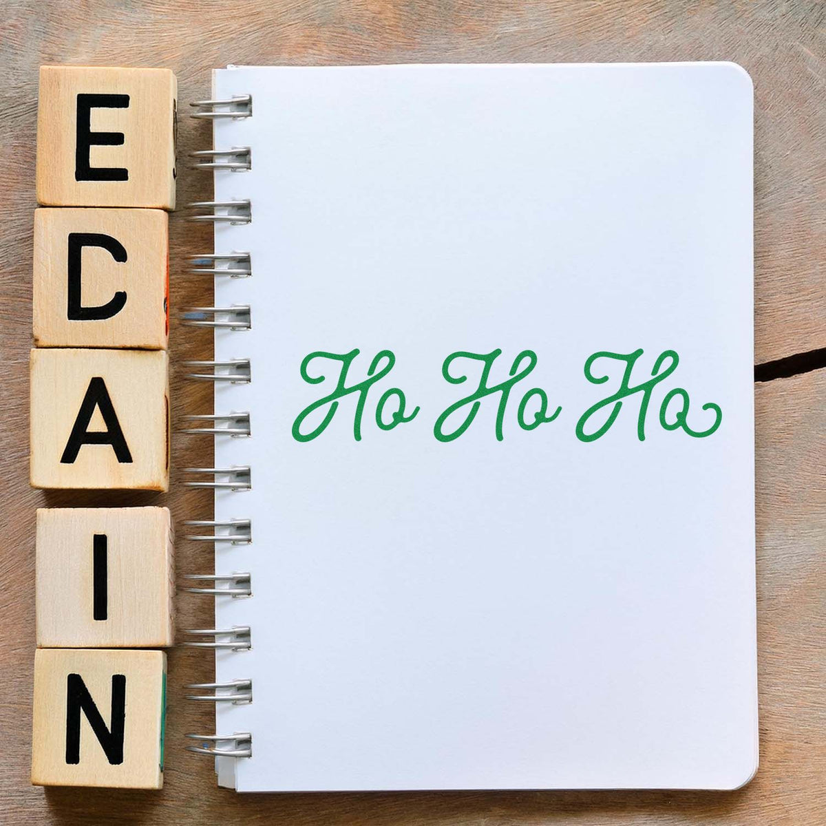 Wooden alphabet stamps beside a white spiral notebook with green Ho Ho Ho seal.